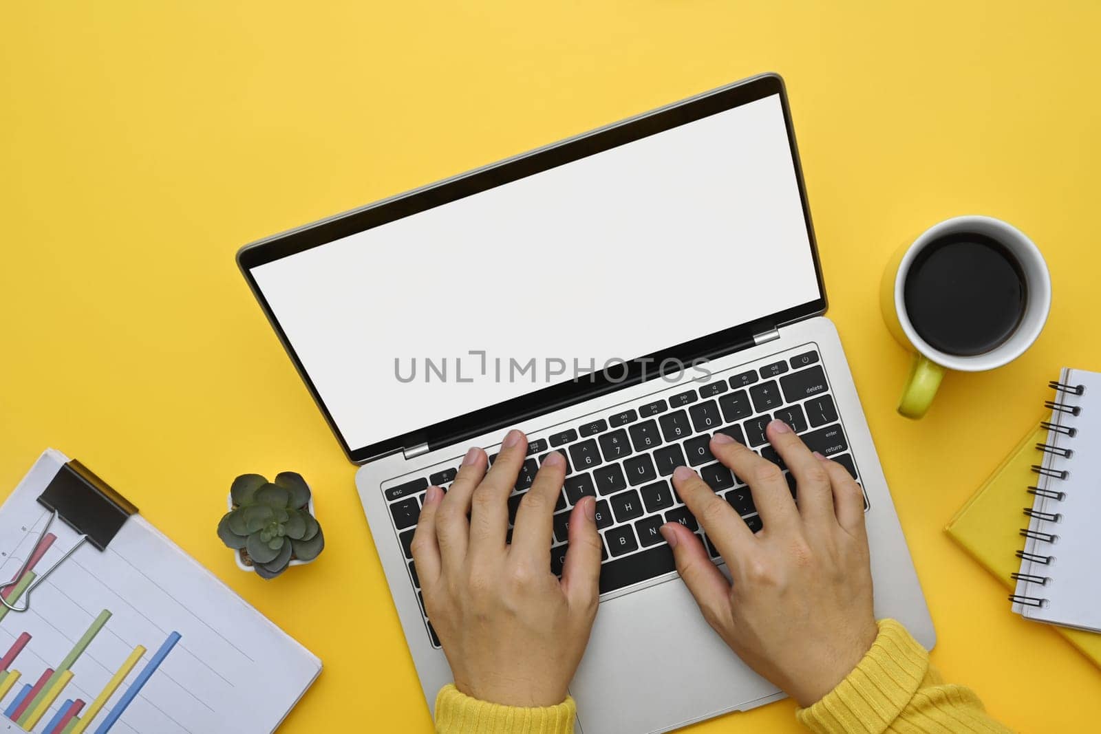 Above view unrecognizable woman hands typing on laptop keyboard over yellow background.