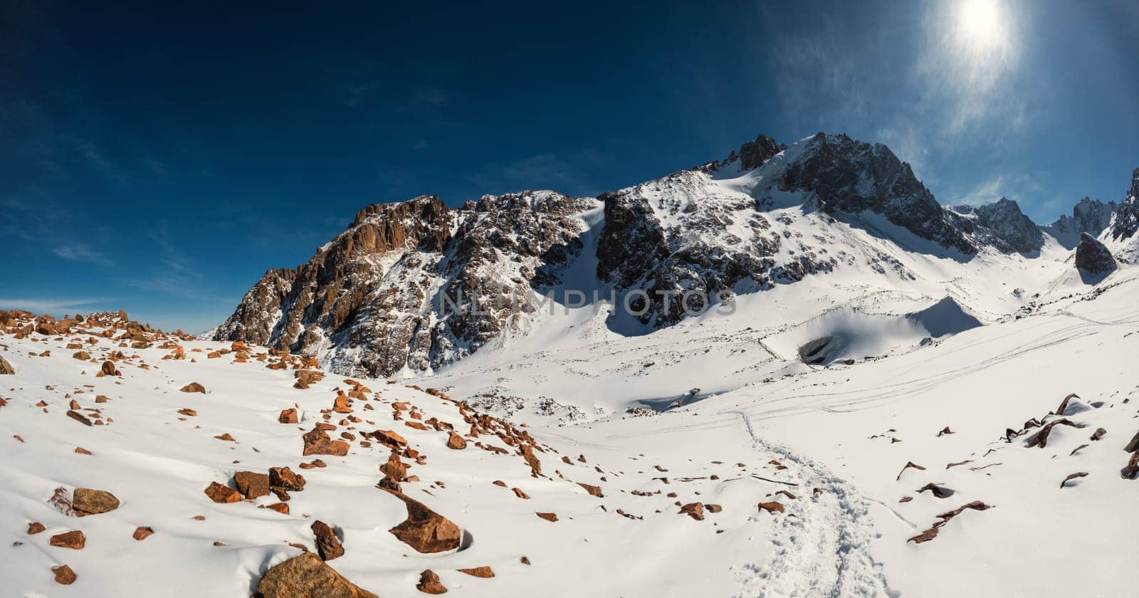 Discover the breathtaking beauty of Central Asia with a panoramic view of the Bogdanovich Glacier in Kazakhstan's Almaty Mountains. This scenic shot captures the winter wonderland on a sunny day.