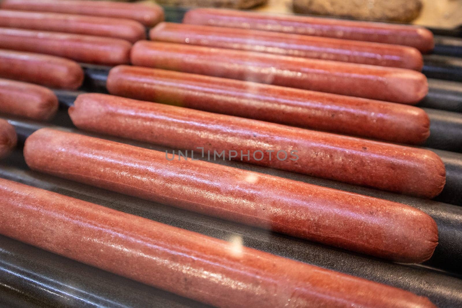 Long sausages are fried on a rotating grill for French dogs or hot dogs in a roadside fast food cafe, popular street food.