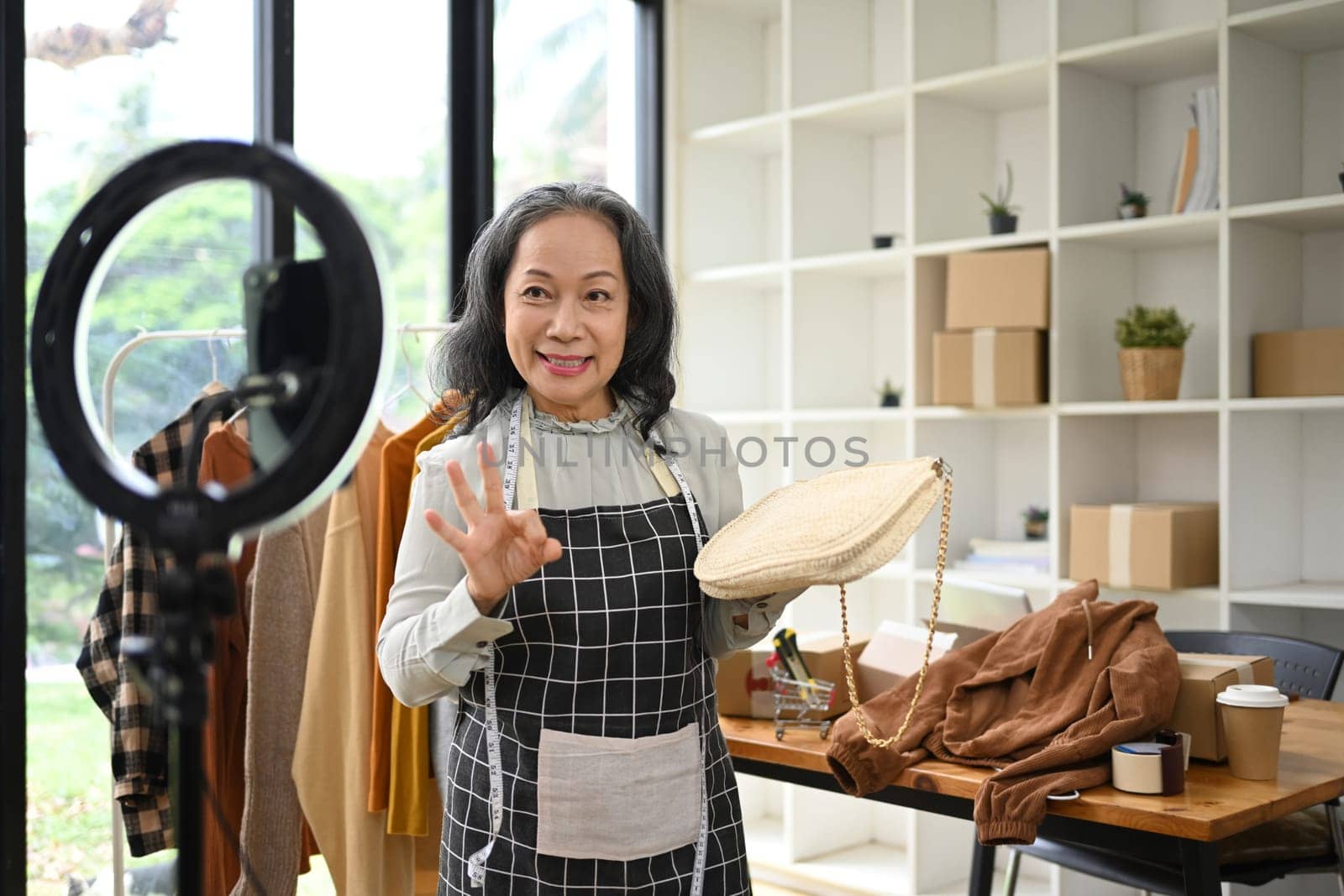 Middle age asian woman presentation bag fashion in front of the camera while live streaming at her shop.