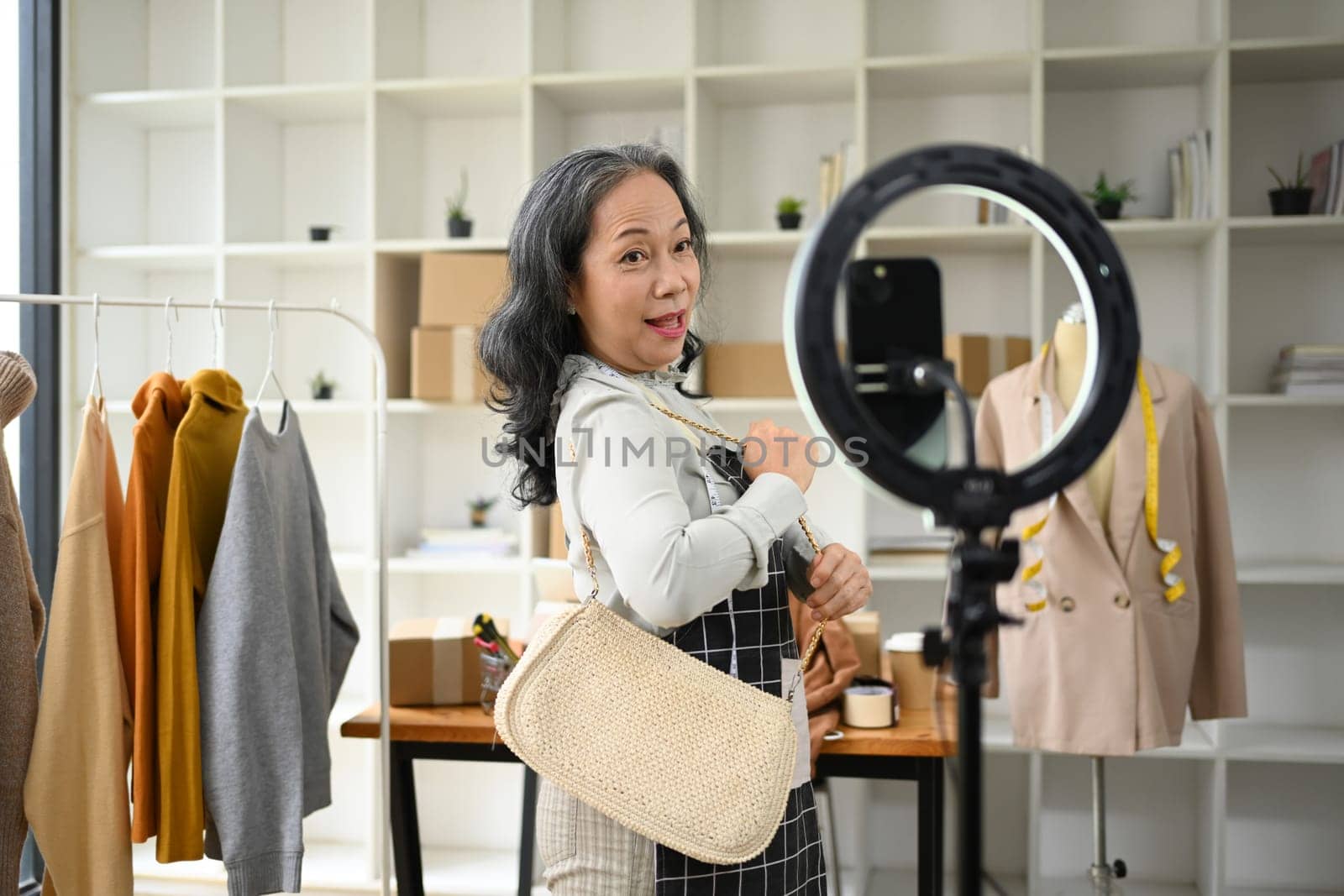 Smiling small business owner live streaming and showing clothing to customer at her shop.