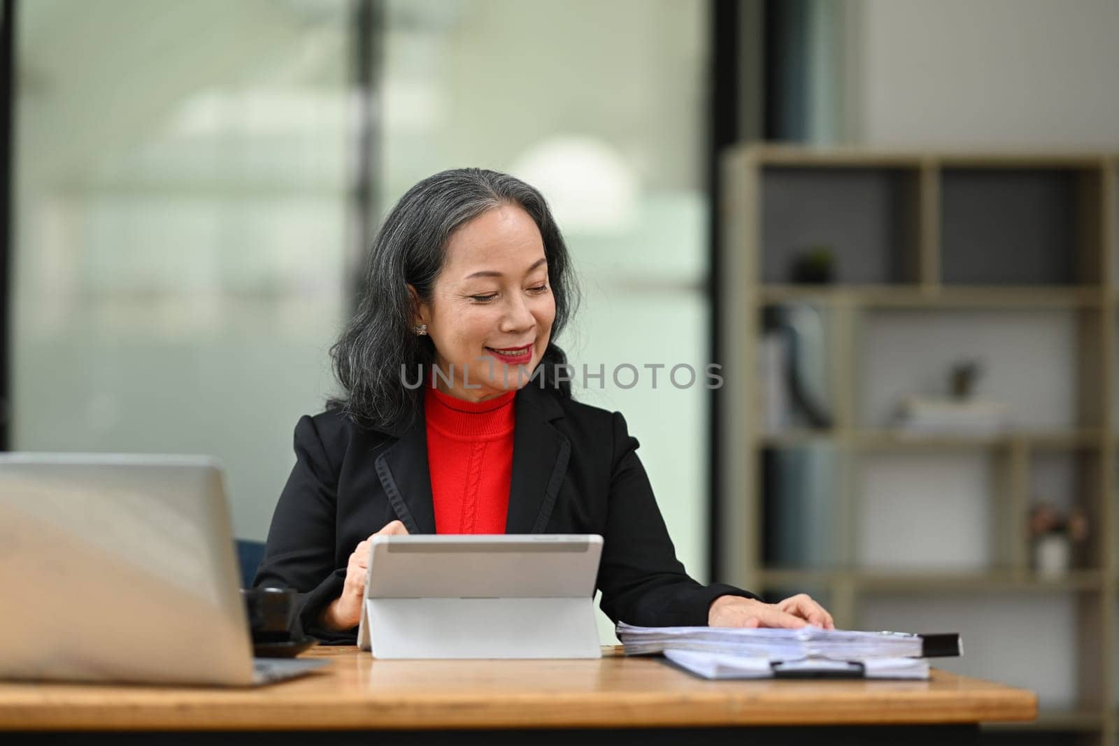 Professional middle age businesswoman working with document and digital tablet at office.