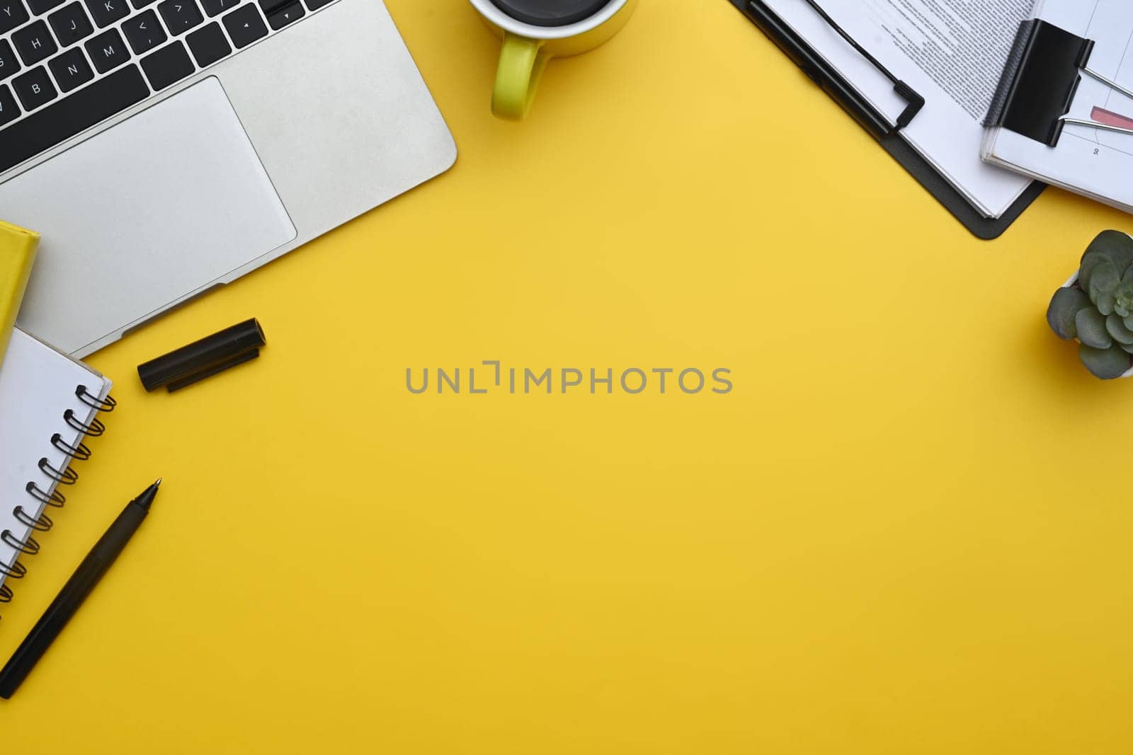 Laptop, notepad, coffee cup and financial reports on yellow background. Top view with copy space.