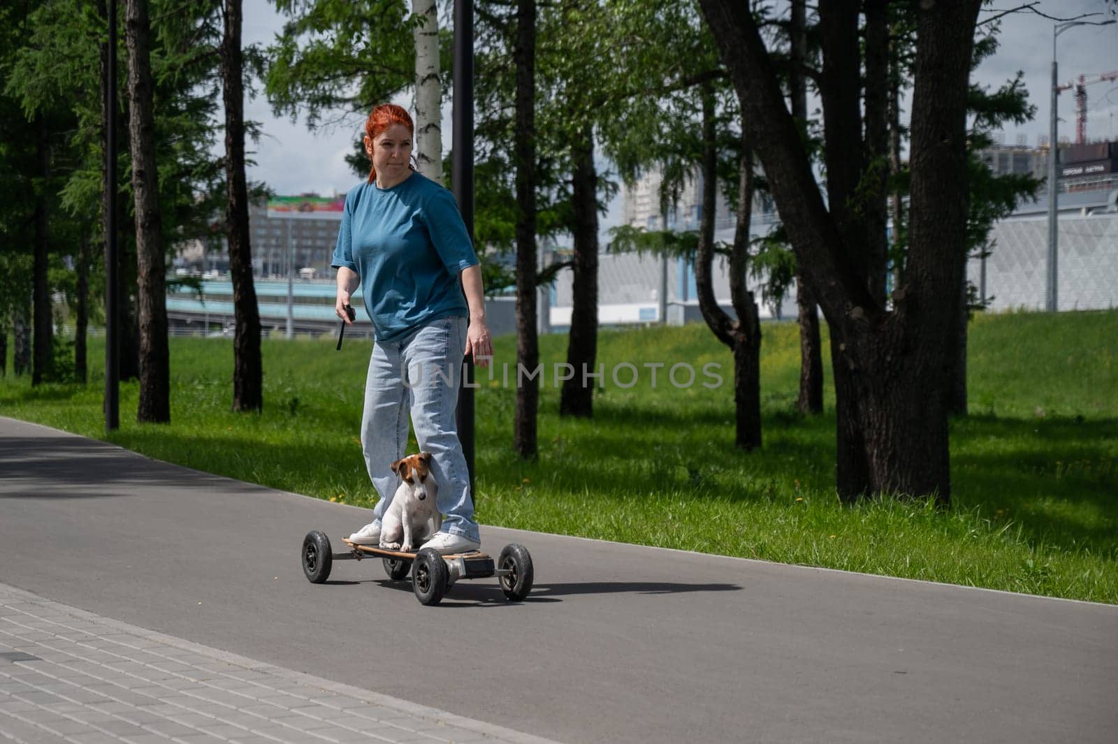 Caucasian woman rides an electric longboard with her Jack Russell Terrier dog