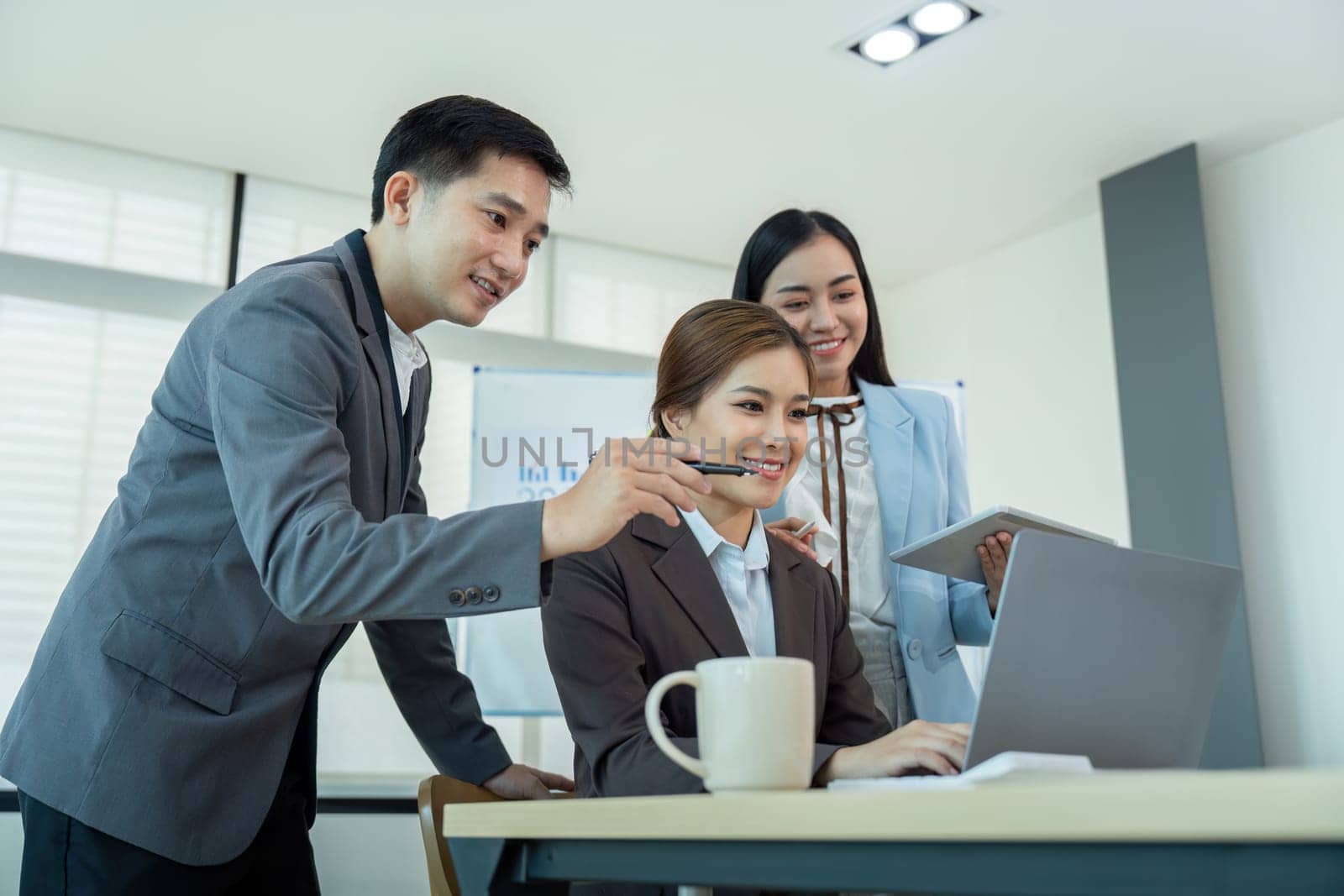 Three business colleagues in formal attire working together on a laptop during an office meeting, showcasing teamwork and corporate collaboration