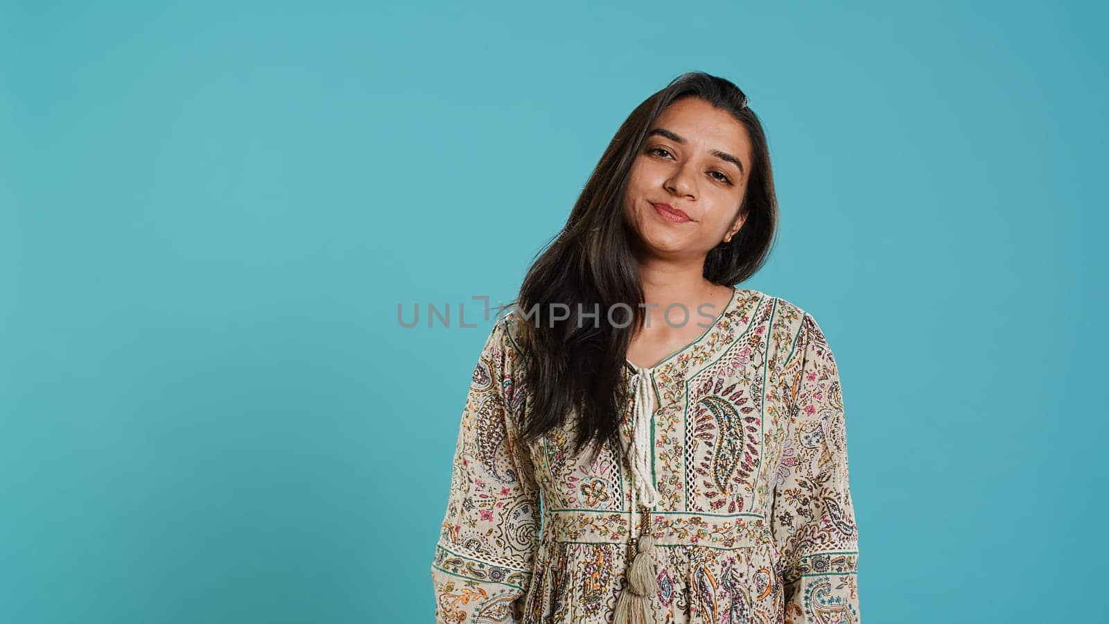 Portrait of cheerful friendly indian woman smiling, flipping long healthy hair, isolated over studio background. Happy brunette person confident with natural hairstyle, feeling satisfied, camera A