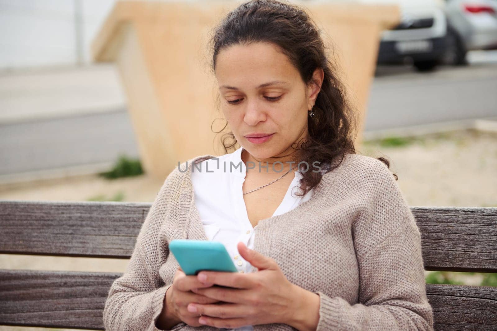 Portrait of a woman using mobile phone outdoors, sitting on a city bench