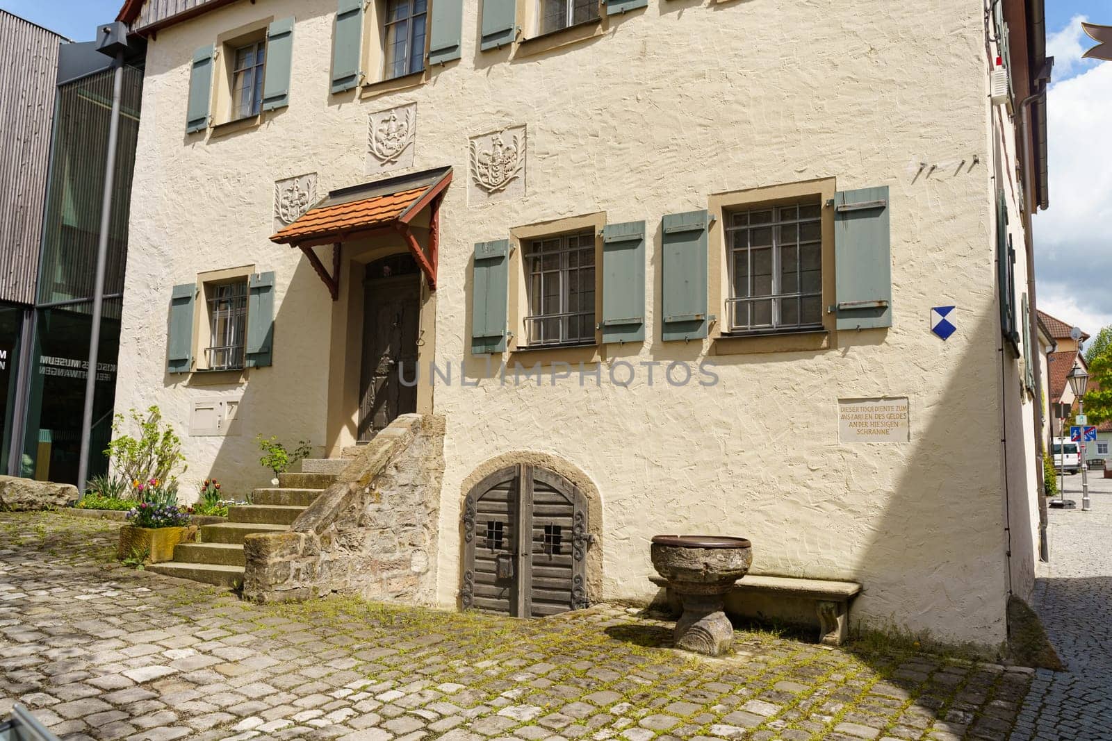Feuchtwangen, Germany - June 6, 2023: A white-washed building with wooden doors and stone steps, located in a cobblestone courtyard in Germany.