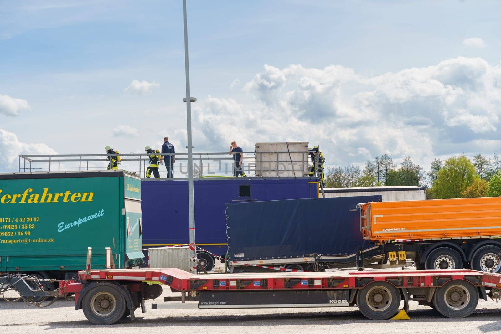 Feuchtwangen, Germany - June 6, 2023: Firefighters practice rescue techniques on a flatbed truck, surrounded by other large trucks in an open area.