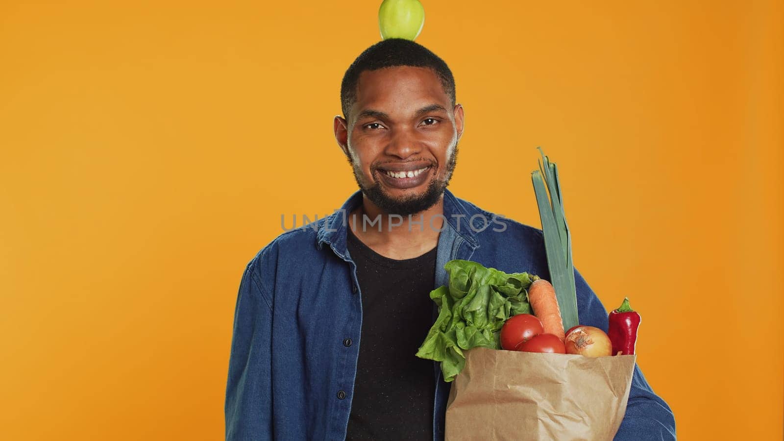 Young adult trying to keep balance with an apple on his head in studio by DCStudio