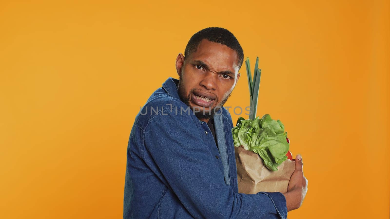 Vegan person acting overprotective of his eco friendly groceries bag, protecting his freshly harvested goods in studio. Serious man taking care of his bio organic belongings. Camera A.