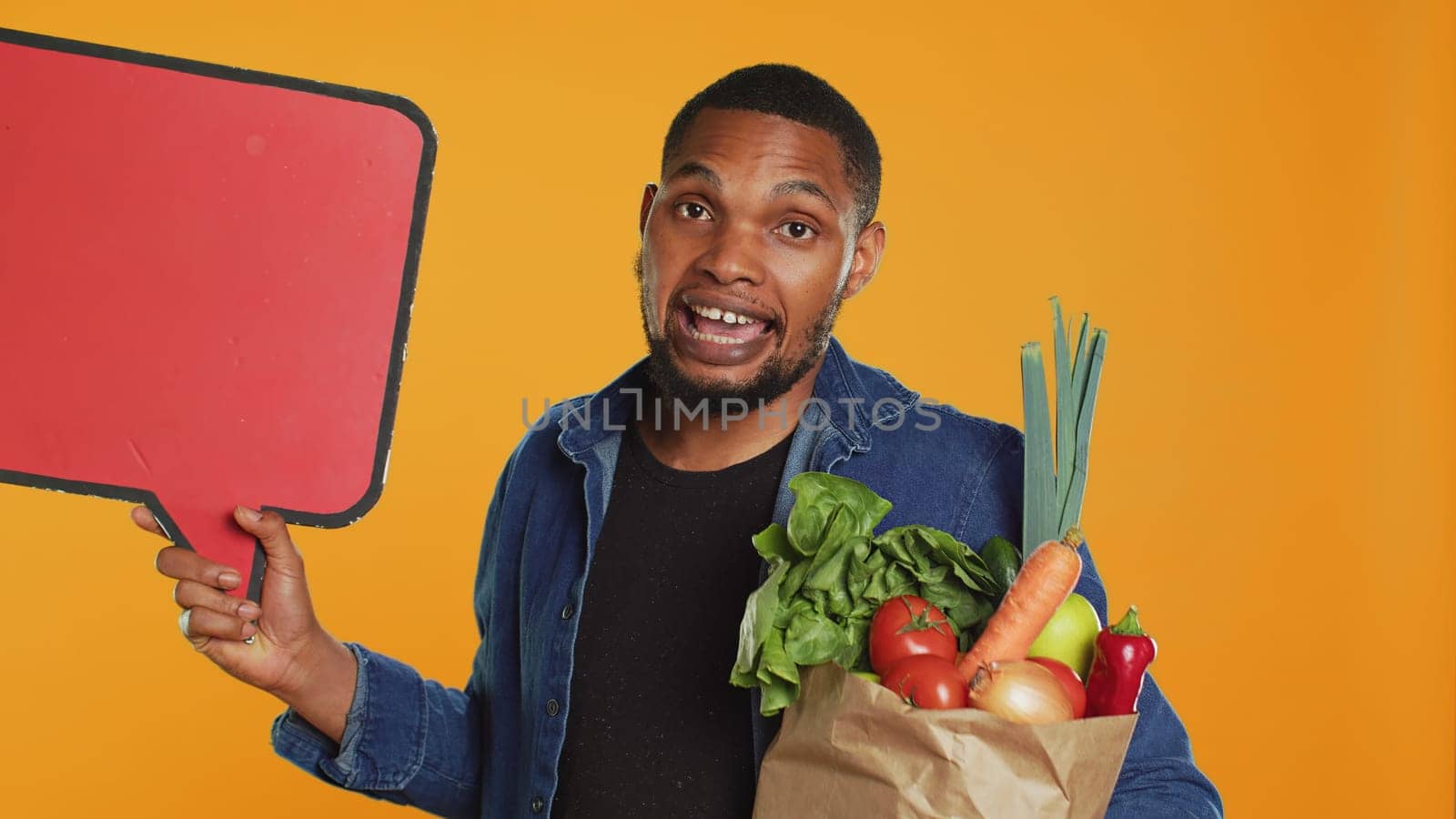 Young man showing a speech bubble empty cardboard sign to create an ad for sustainable lifestyle healthy eating. Guy doing a promotional advertisement for bio ripe fruits and veggies. Camera A.