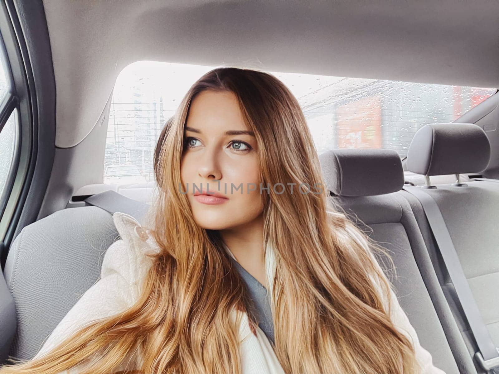 Young woman with long hair, wavy hairstyle in the car or taxi cab as passenger, exploring the city, transport and travel by Anneleven