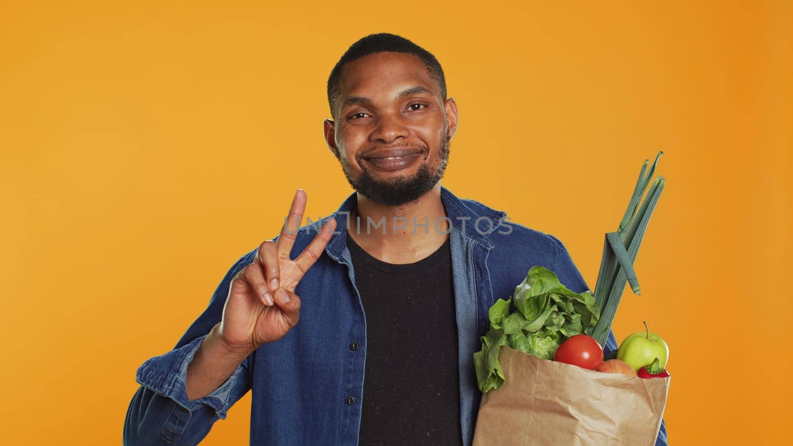 Young adult showing peace sign gesture and holding organic groceries by DCStudio