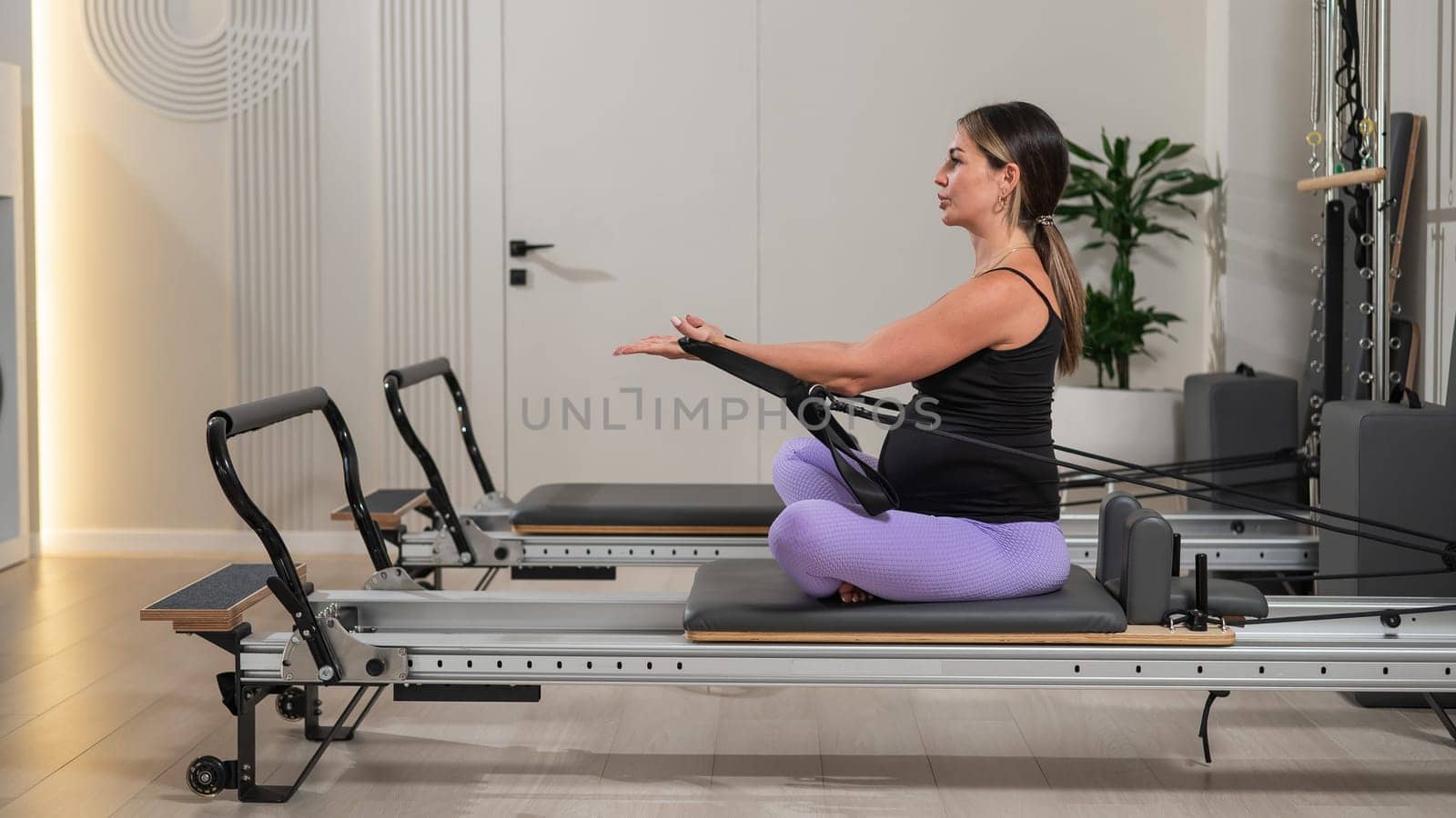 Pregnant woman doing Pilates exercises on a reformer machine. by mrwed54