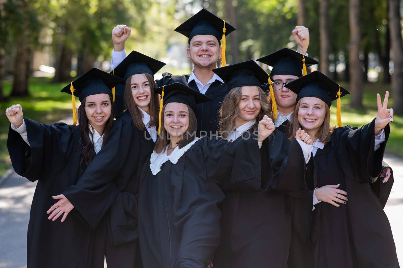 Group of happy young people in graduation gowns outdoors. Students are walking in the park. by mrwed54