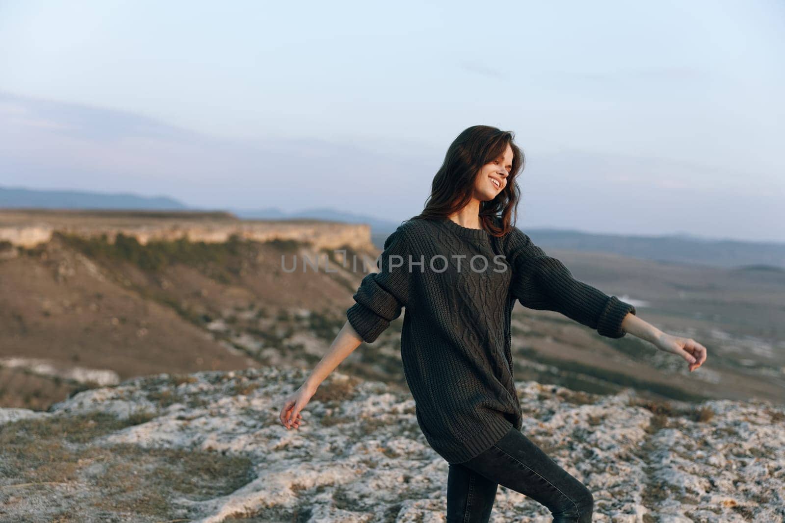 Woman in sweater standing on hill with outstretched arms gazing at sky in peaceful solitude