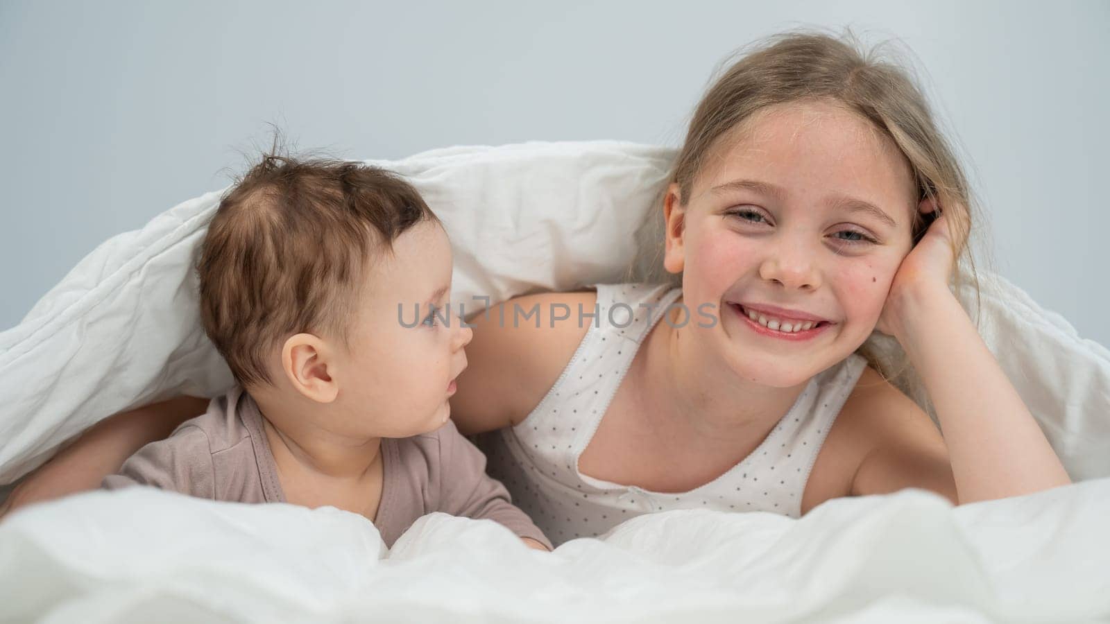 Little girl and her newborn brother hiding under the blanket