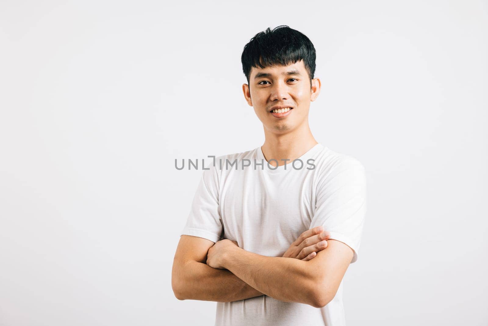 A portrait of a happy young Thai man exuding confidence and a friendly smile, standing with crossed arms. Studio shot isolated on white, portraying positivity and success.