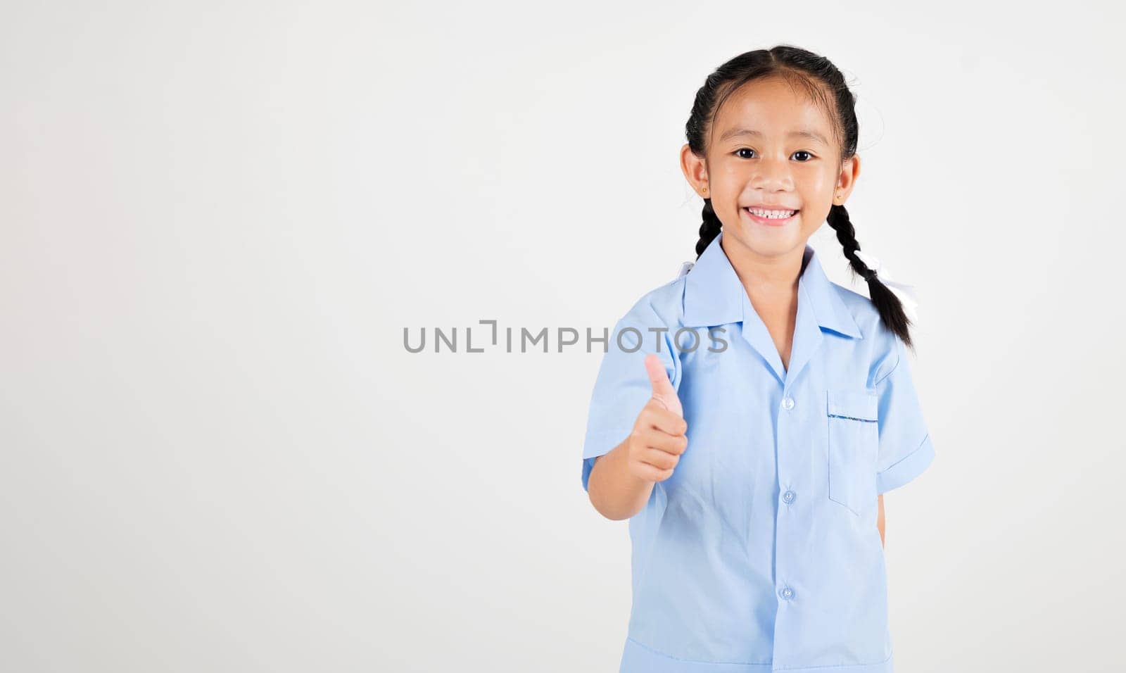 Portrait smiling Asian little girl kindergarten giving thumbs up studio shot isolated white background, good job feedback, woman kid wearing school uniform by Sorapop