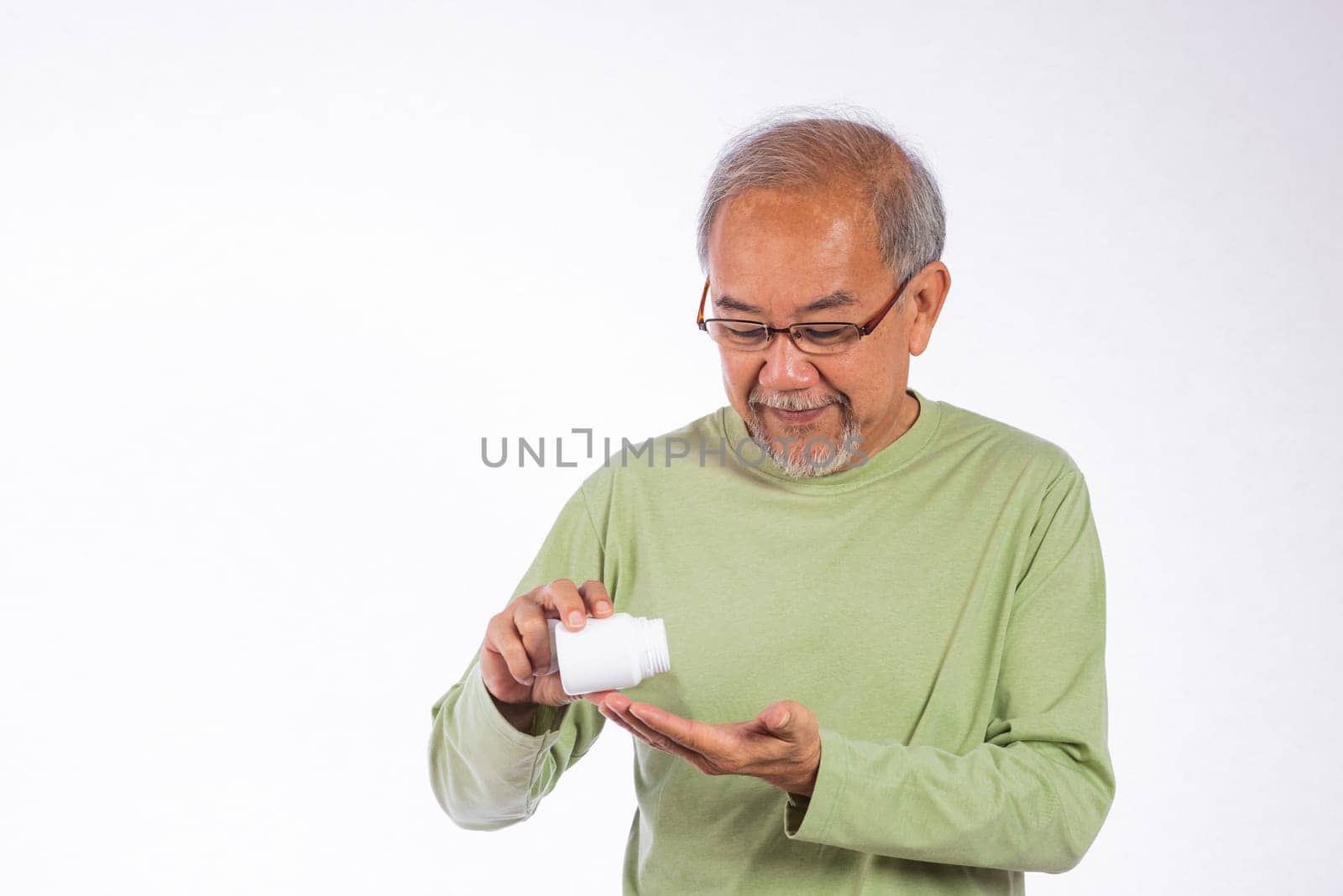 Portrait Asian older man is holding a white pill bottle and spilling in his hand studio shot isolated on white background. He is smiling and he is happy, senior man frug medicine bottle