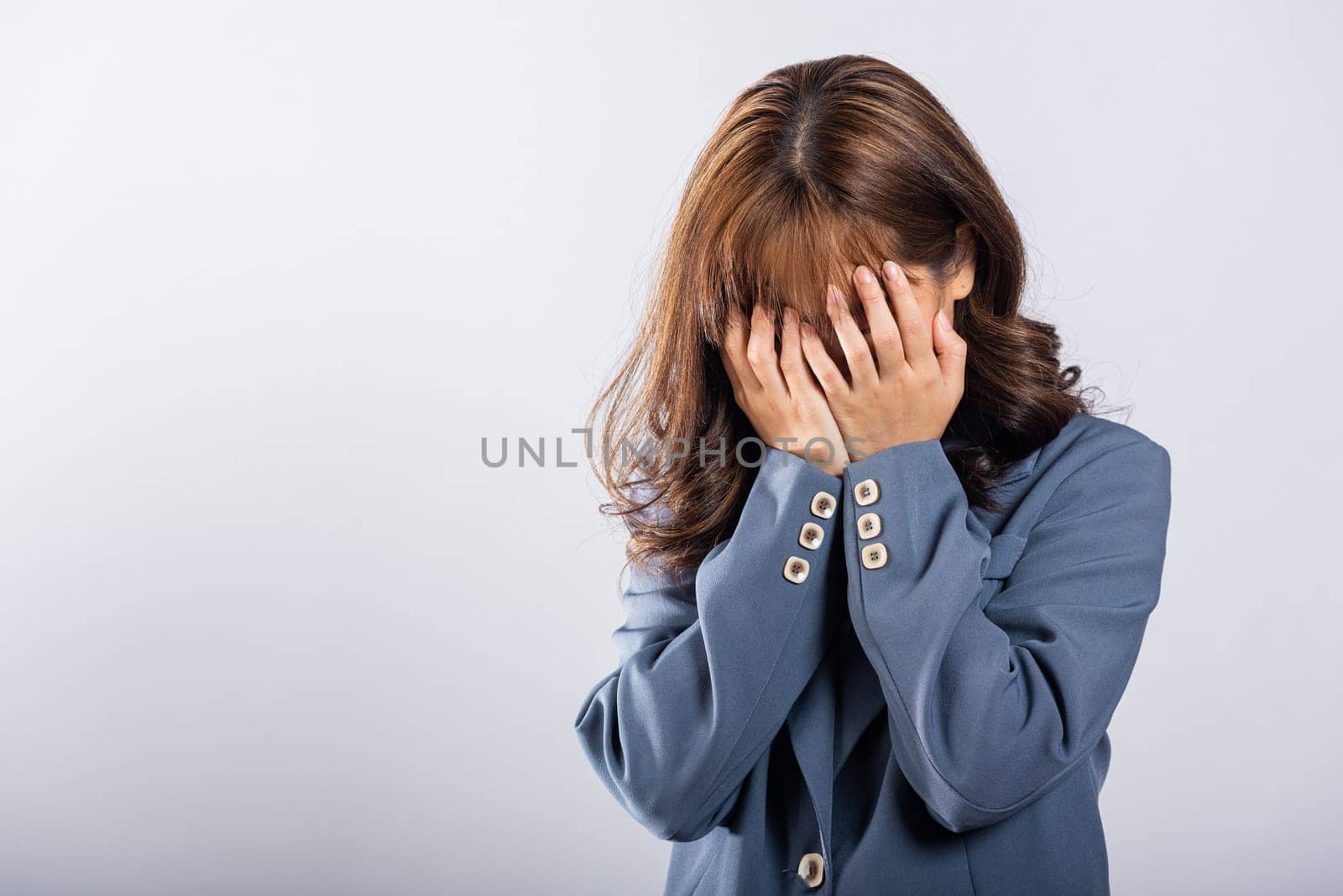 Asian woman's emotional turmoil is evident as she cries and wipes away tears with her fingers. Isolated on white, her expressive face conveys powerful story of sadness and despair.