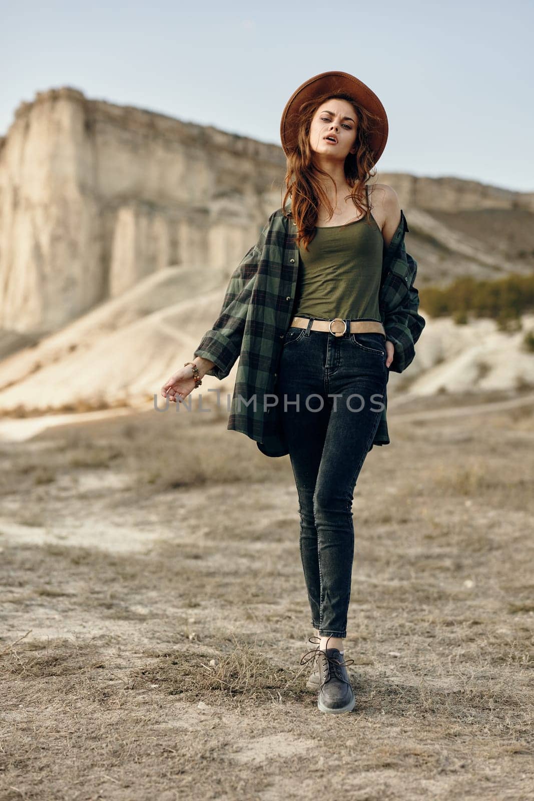 Serene young woman in plaid shirt and hat admires stunning desert landscape with mountains afar