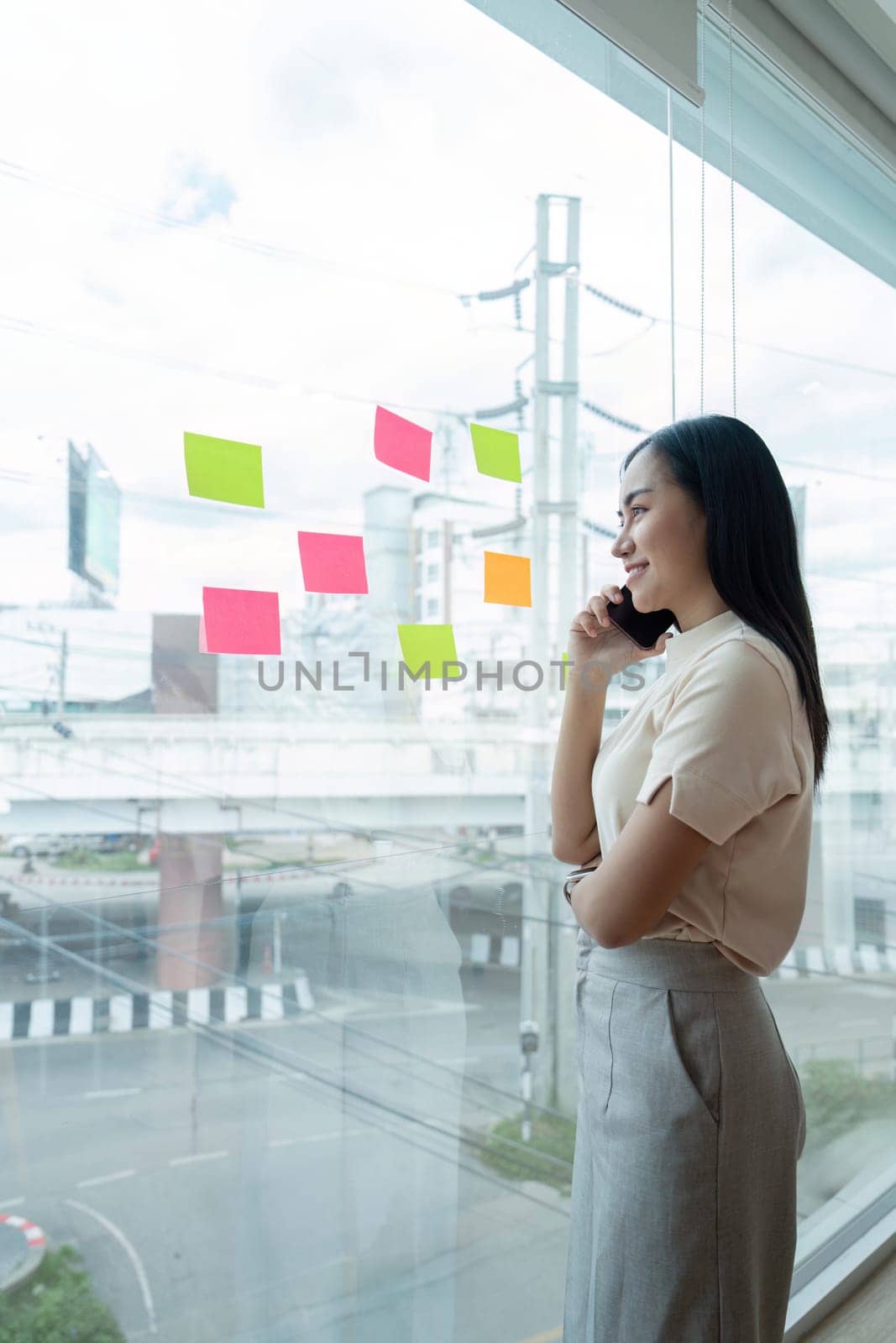 Businesswoman brainstorming ideas while looking at sticky notes on a window in a modern office setting, focusing on planning and creativity