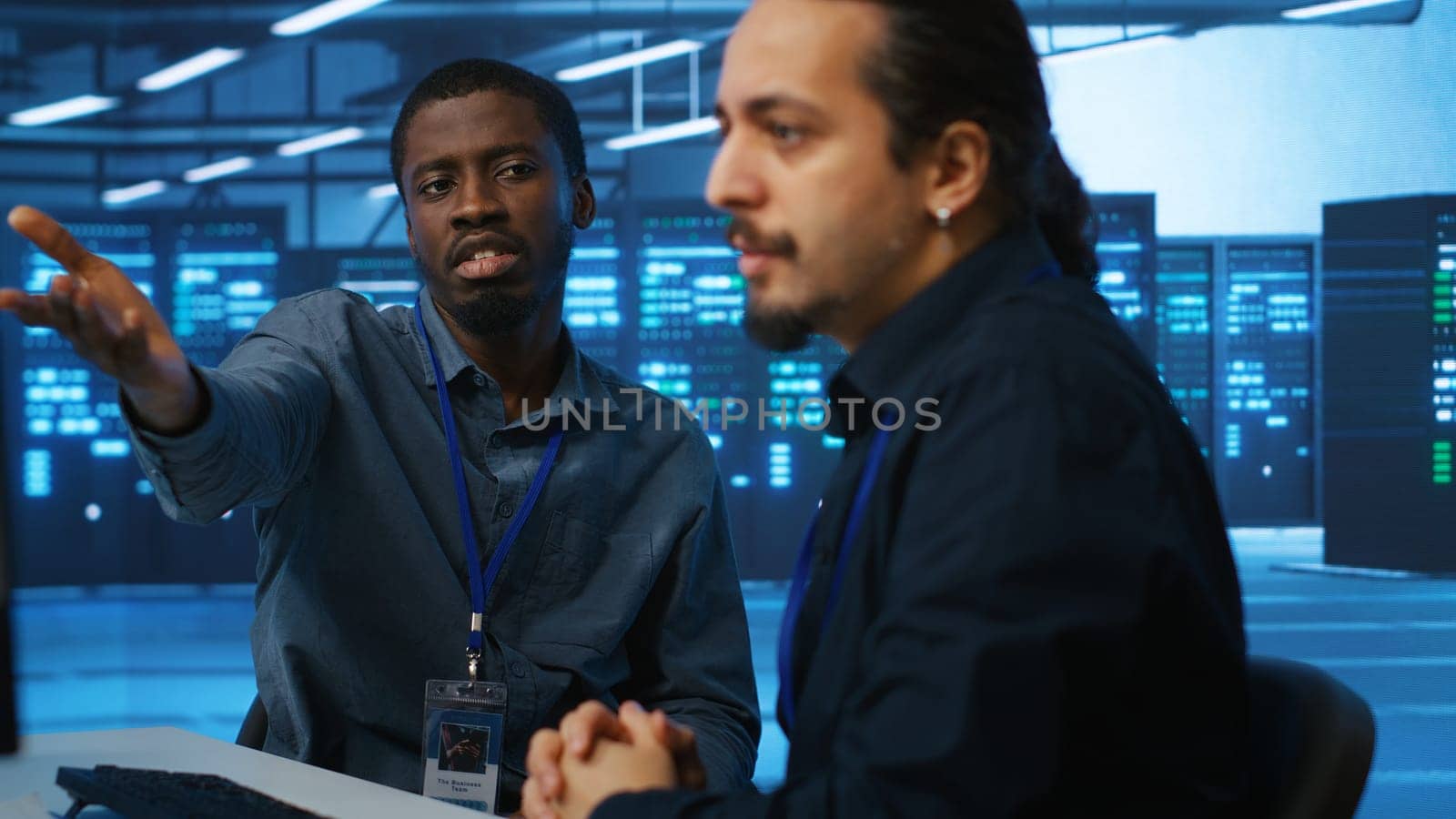 Upbeat african american computer scientist and coworker upgrading equipment in data center. Joyous admin at PC desk in high tech facility overseeing server clusters helped by colleague