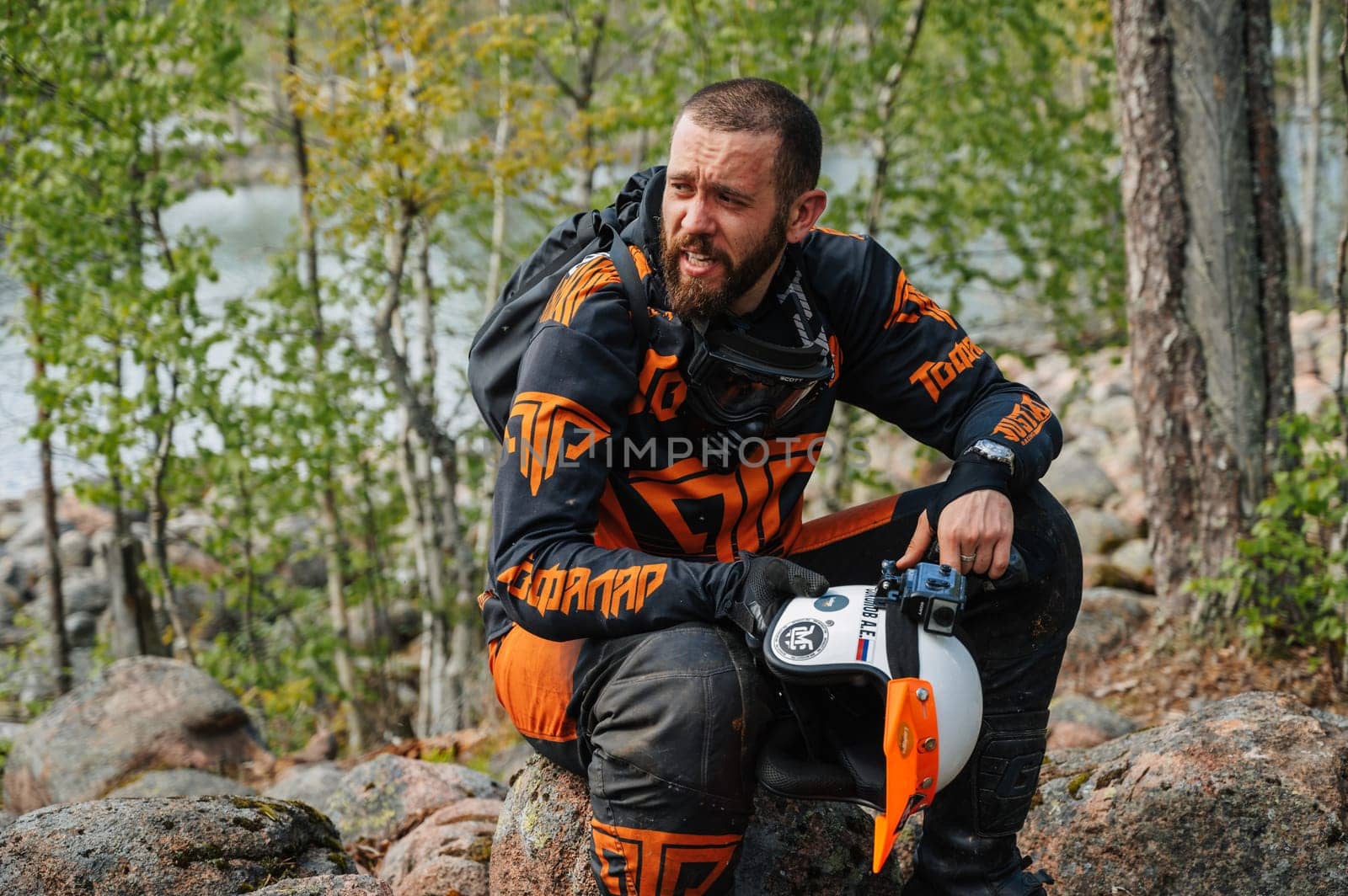 REPUBLIC OF KARELIA, RUSSIA - CIRCA JUNE, 2022: Off-road tournament Ladoga Trophy 2022 in Karelia. A tired sports motorcycle racer is resting in nature during a race