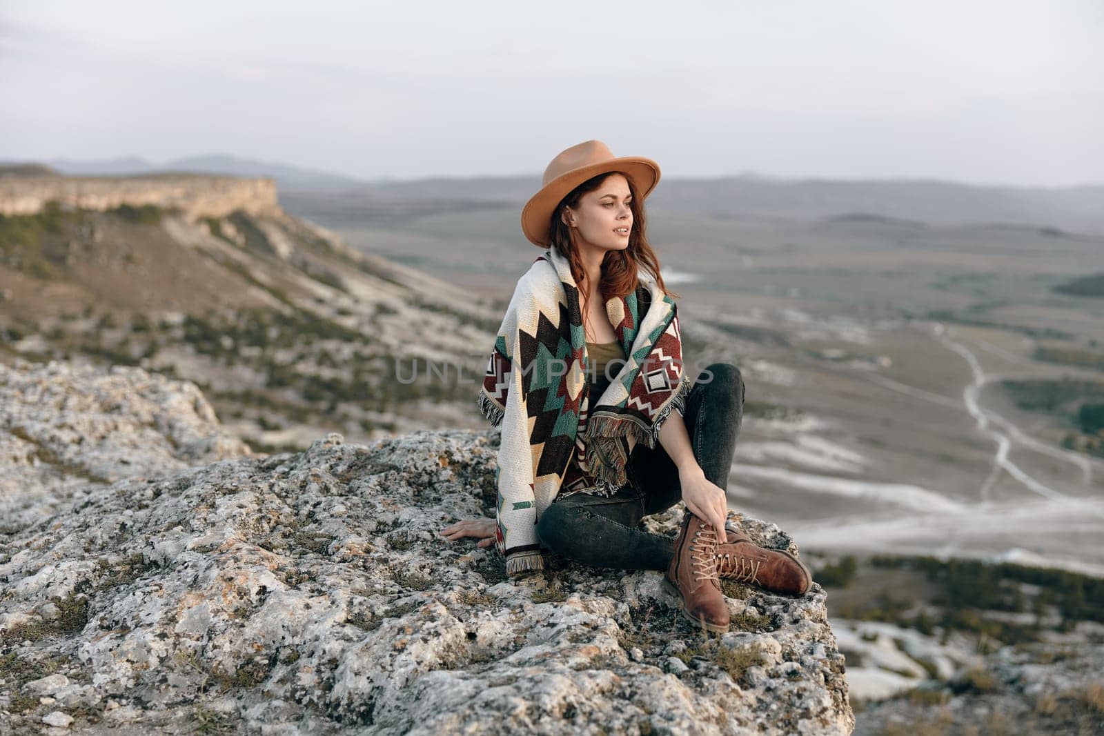 Serene woman in cozy attire sitting with crossed legs on a rock in the wilderness