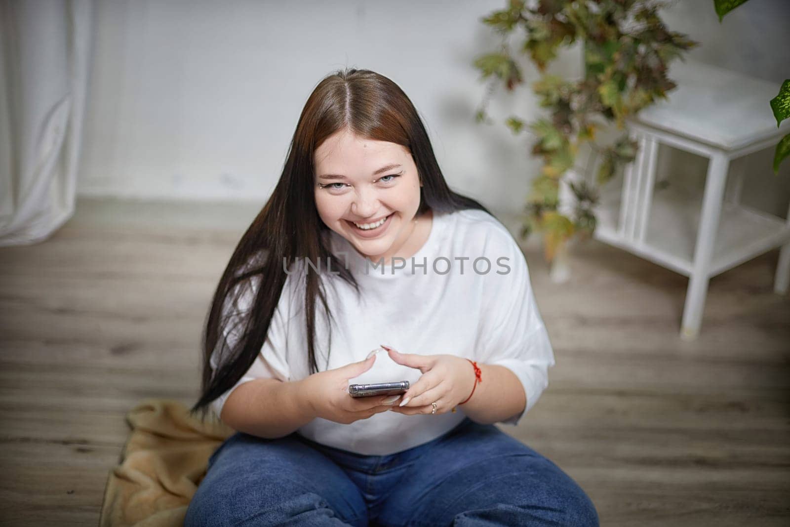 Stylish chubby student brunette girl with cell mobile phone. Attractive young brunette overweight indoors