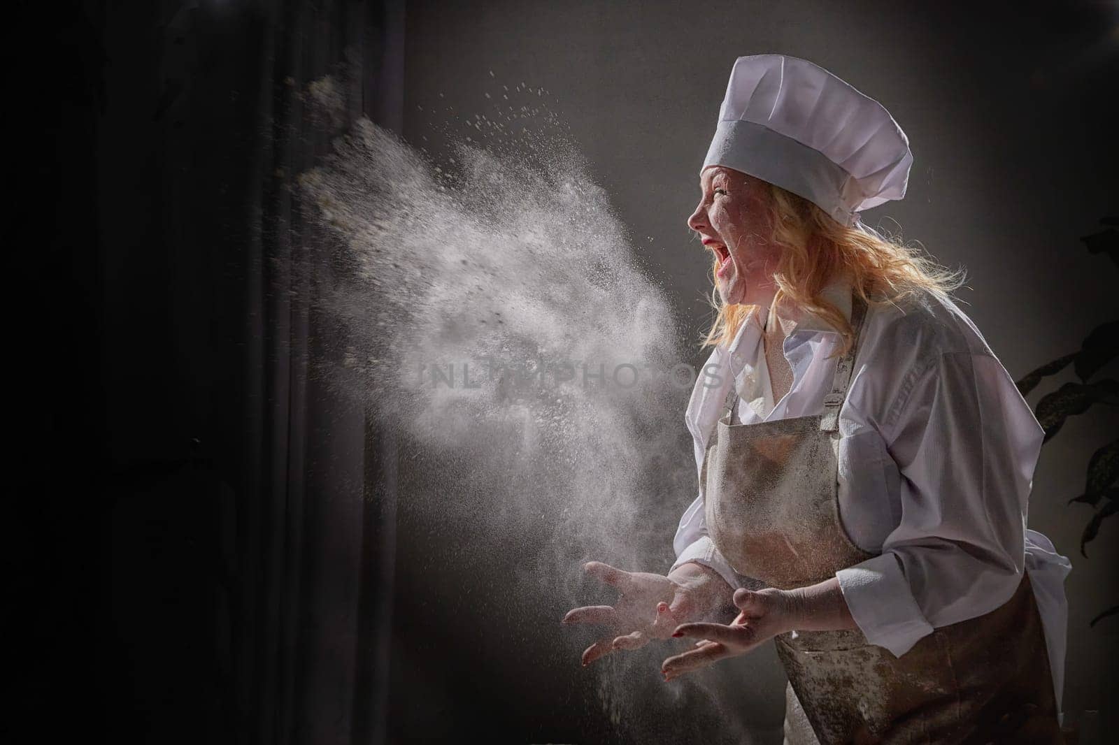 Fat funny female cook in a hat and apron posing and taking selfie in the kitchen with flour. Cooking, body positive, cloud, smoke, flour