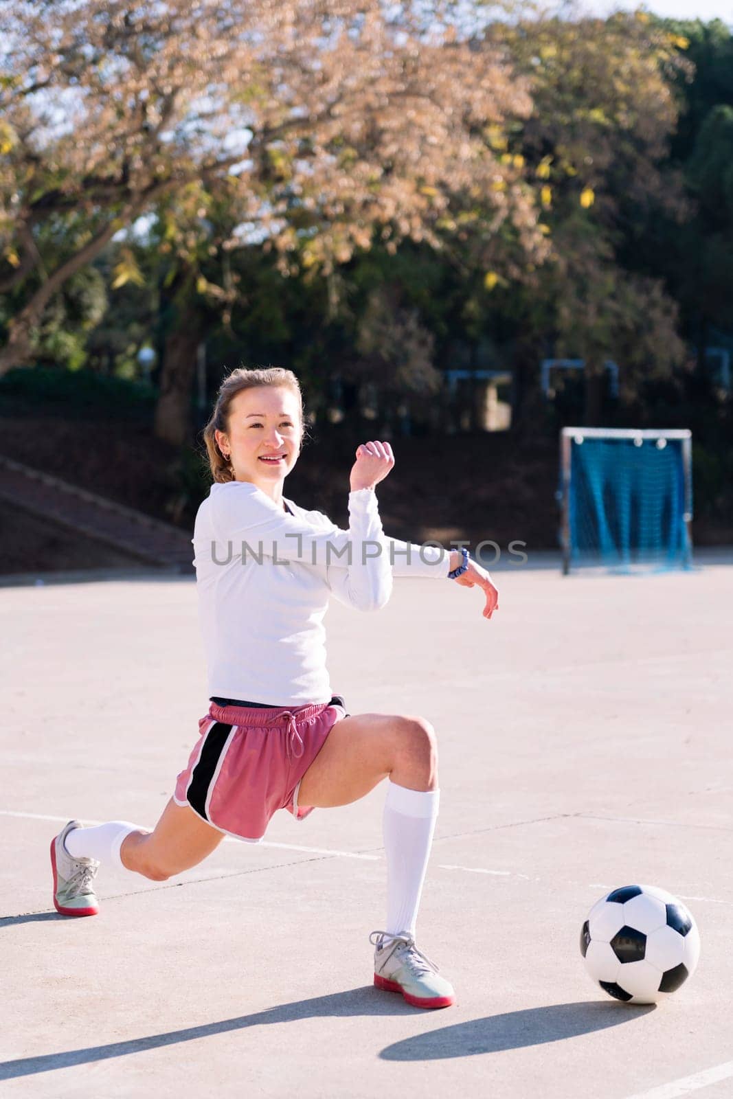 young caucasian woman with a soccer ball stretching arms in a urban football court, concept of sport and active lifestyle