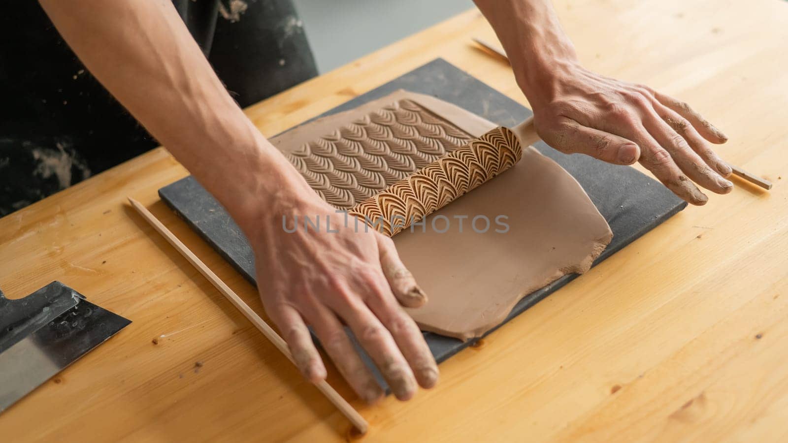 Close-up of a potter's hands rolling out clay using a rolling pin with patterns. by mrwed54