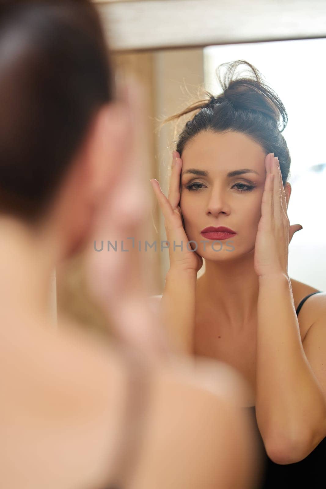 Beautiful young woman brunette watching face closely in front of bathroom mirror