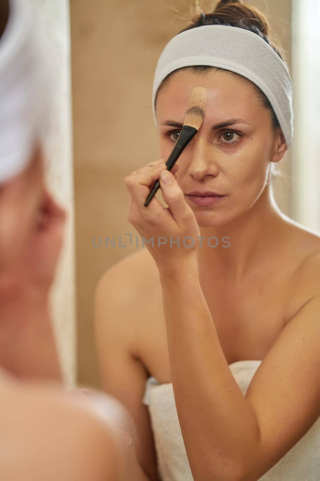 Beautiful young brunette woman applying fluid in front of bathroom mirror