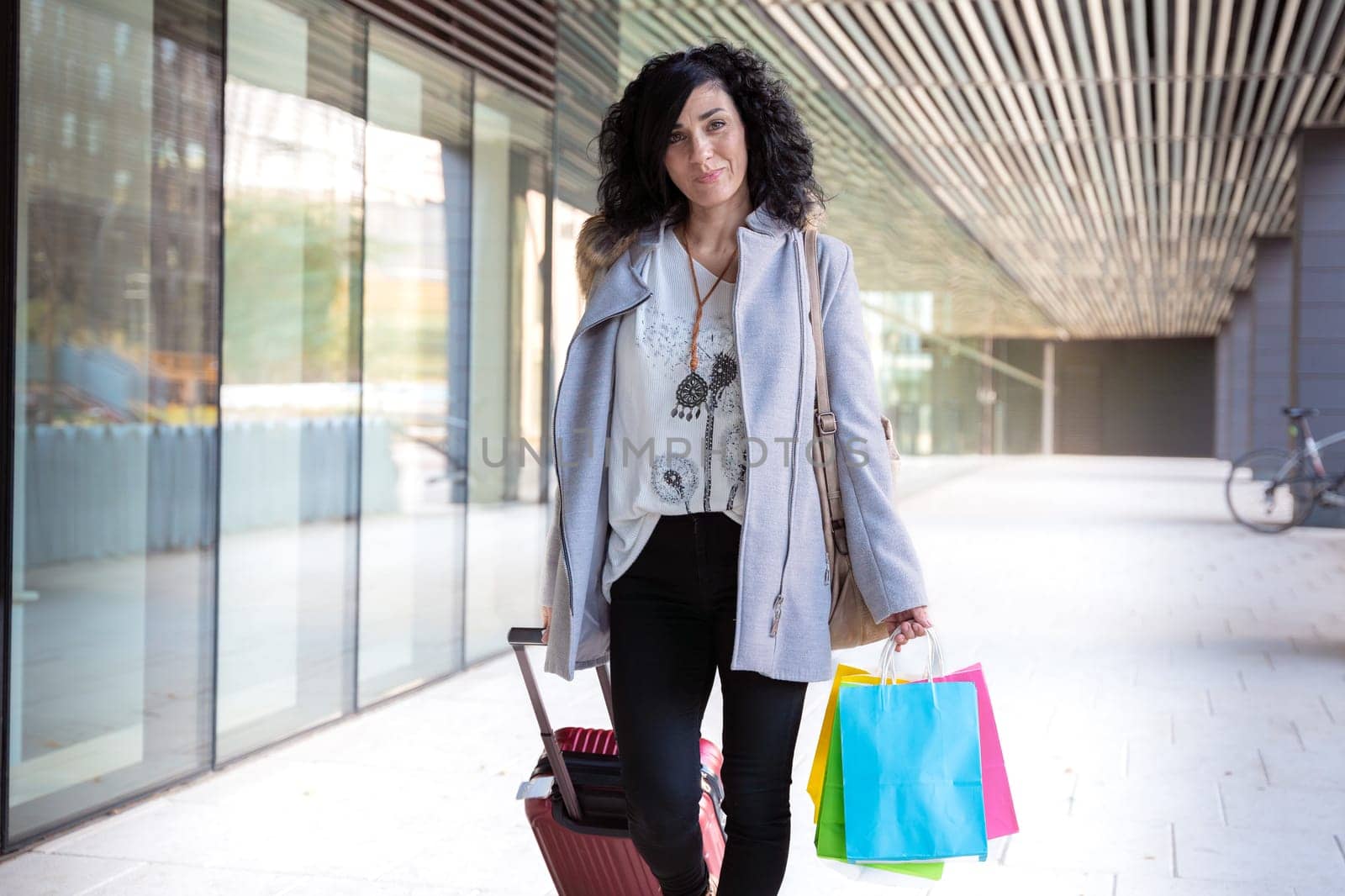 Woman with shopping bags and suitcase walking looking at camera by mariaphoto3