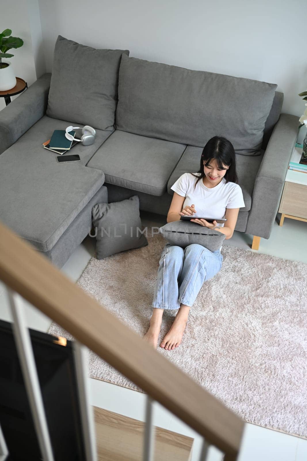 Above view casual young woman sitting on floor in living room and using digital tablet.