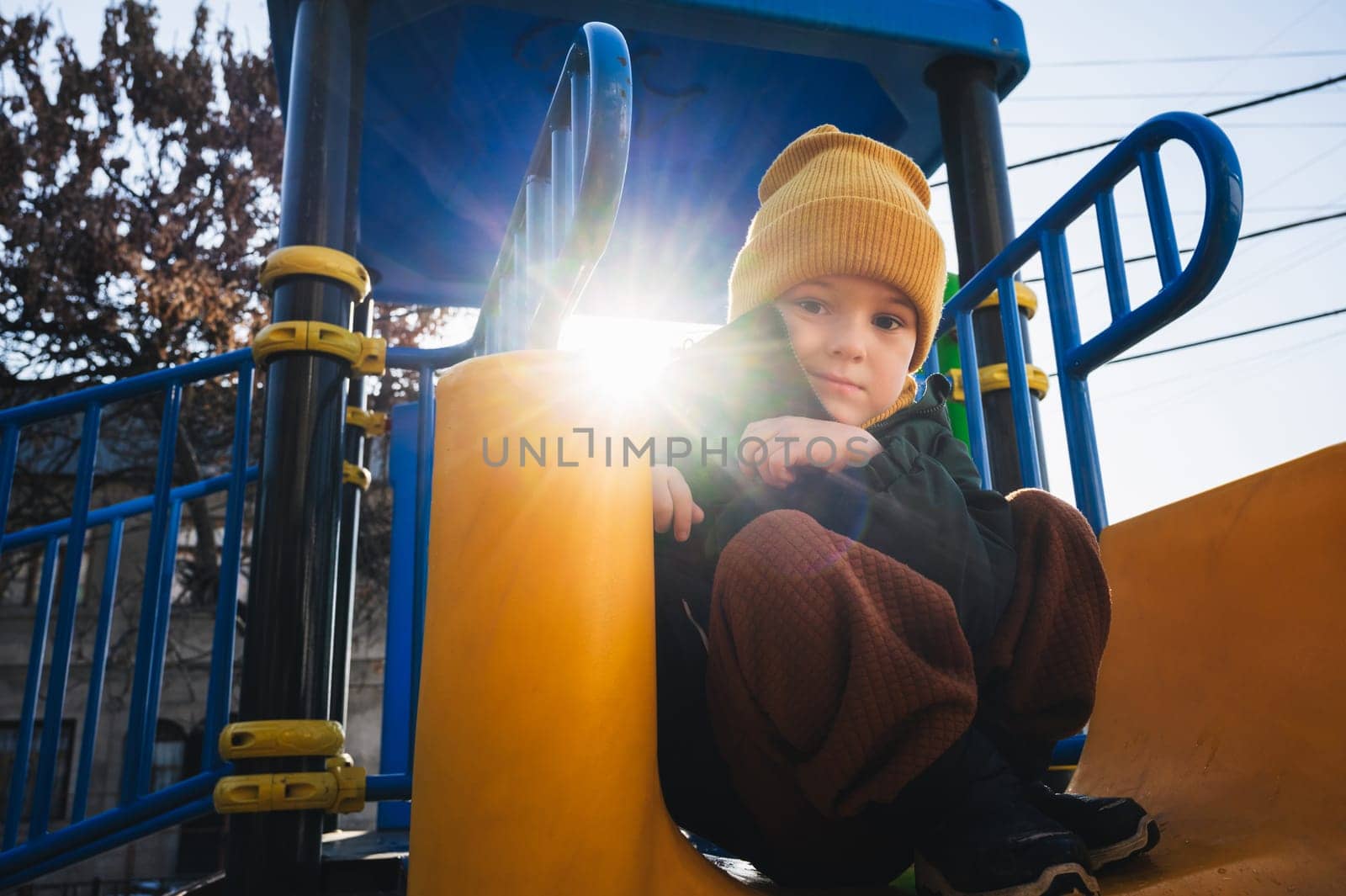 child kid boy play on the playground on the slide in autumn on a sunny day