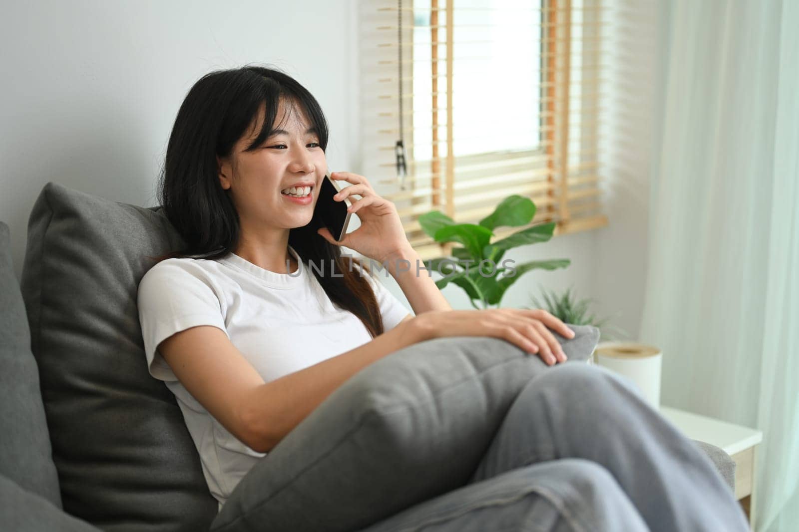 Smiling young woman in casual clothes having g pleasant phone conversation in living room.