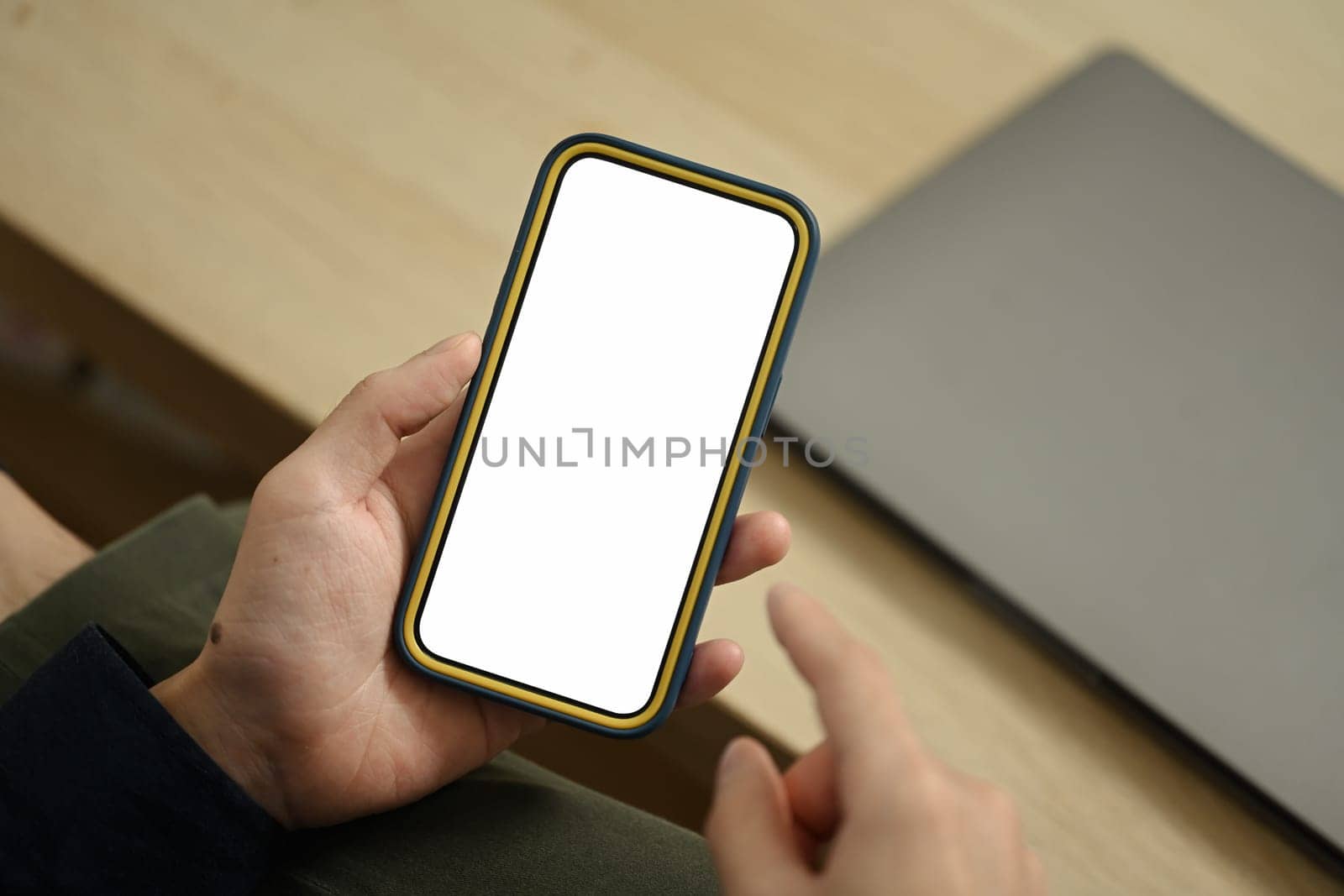 Unrecognizable young man hands holding mobile phone with empty screen sitting on couch.