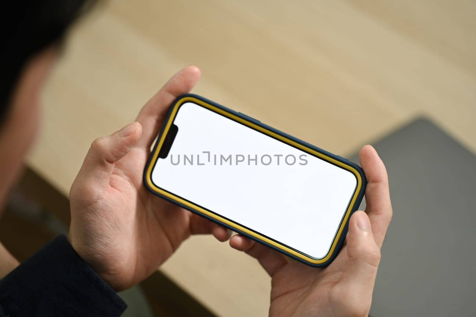 Cropped shot of man holding smartphone with blank screen sitting on couch in living room.