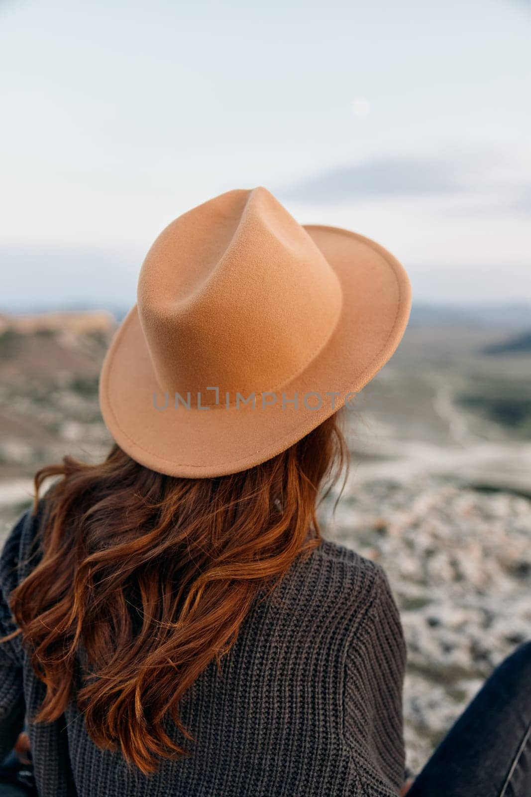 Woman in hat contemplating majestic mountain view from rock perch by Vichizh