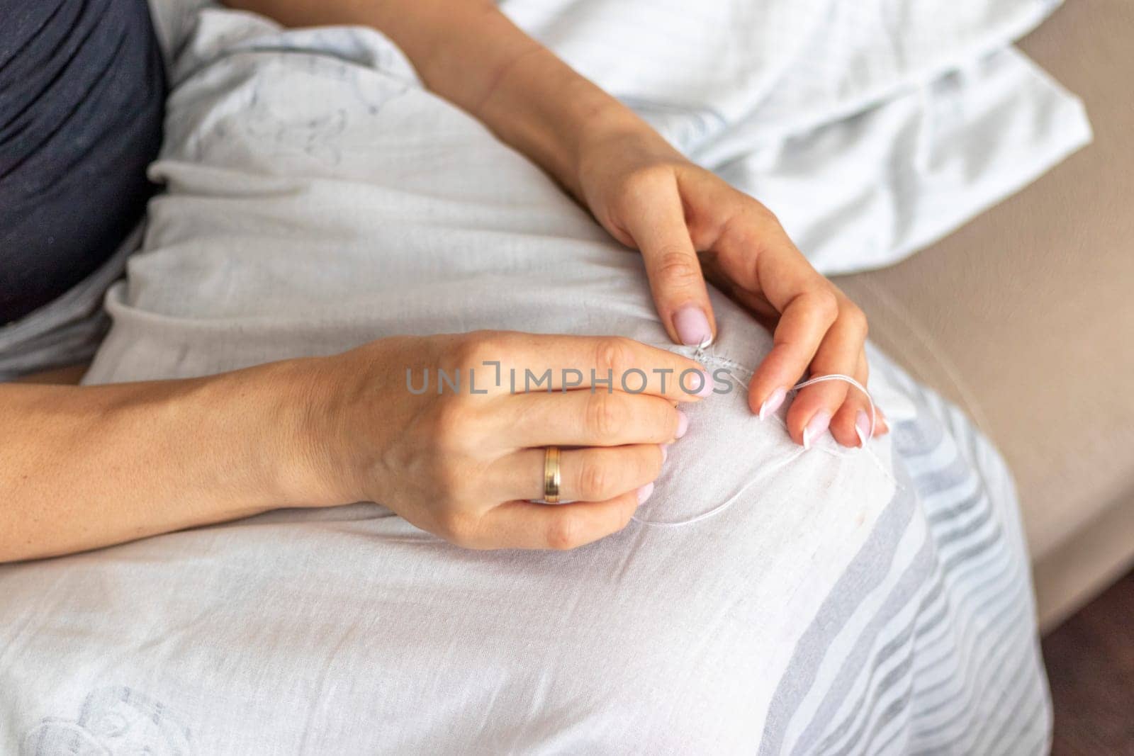 Shot of the woman with beautiful hands stitching up or patching a linen fabric