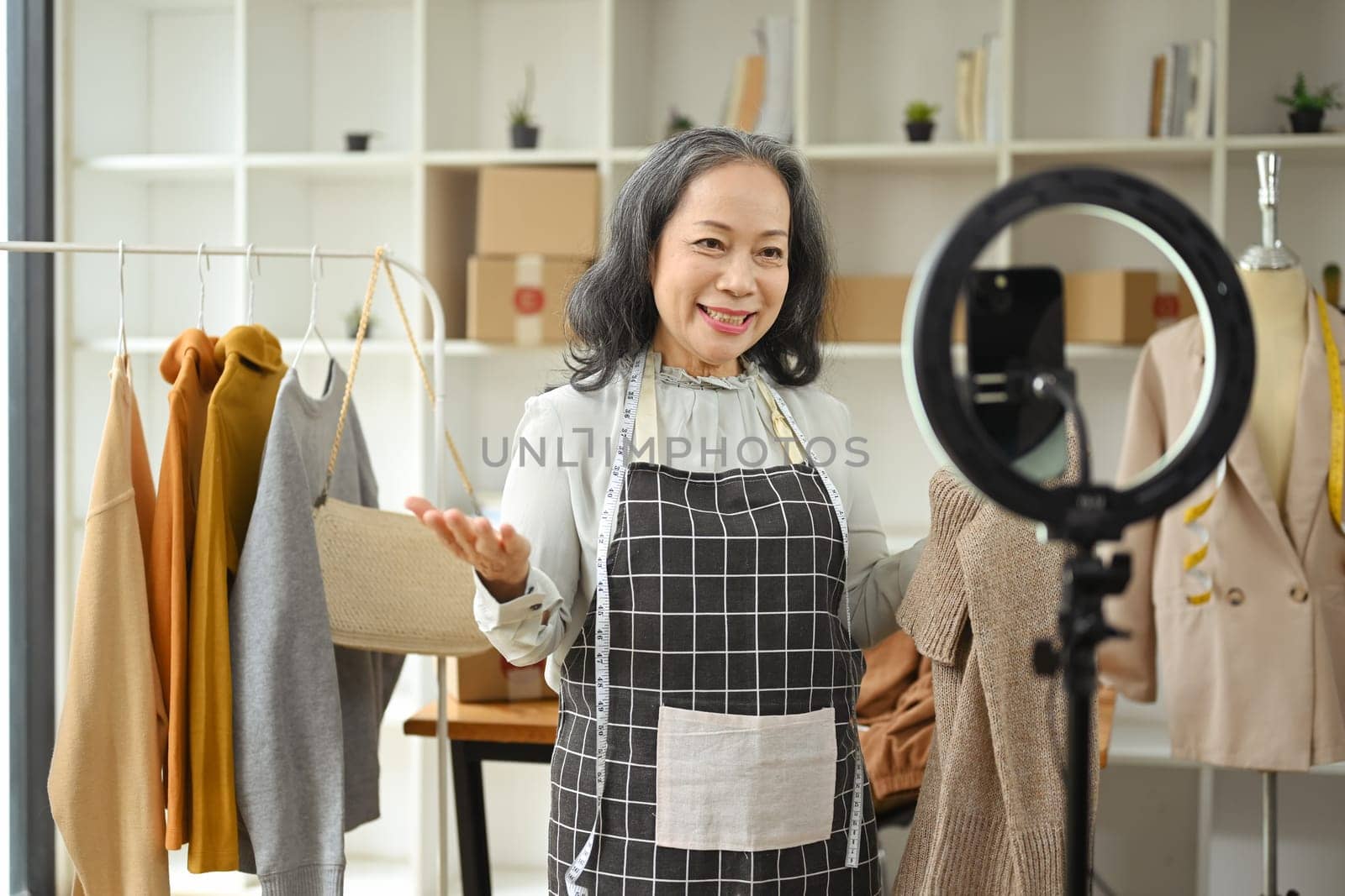 Middle age small business owner using mobile phone live streaming to sell fashion clothes.