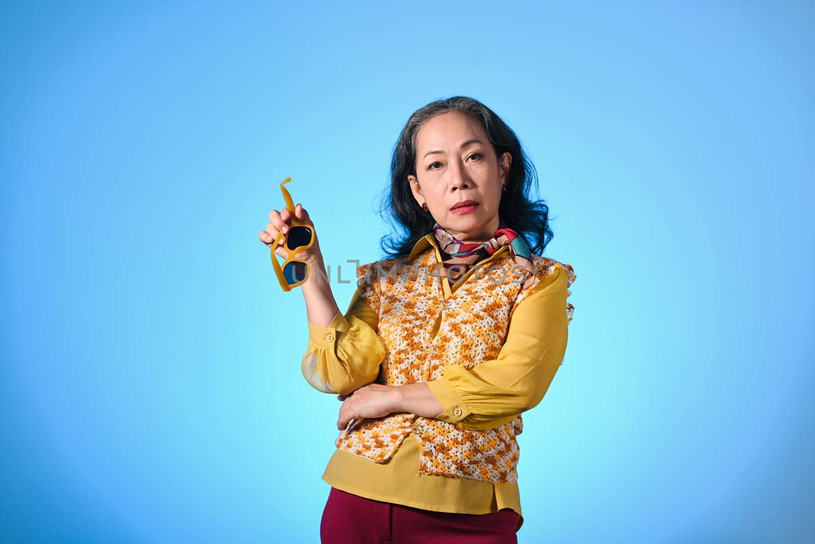 Portrait of confident middle aged woman with stylish outfit posing over blue background.