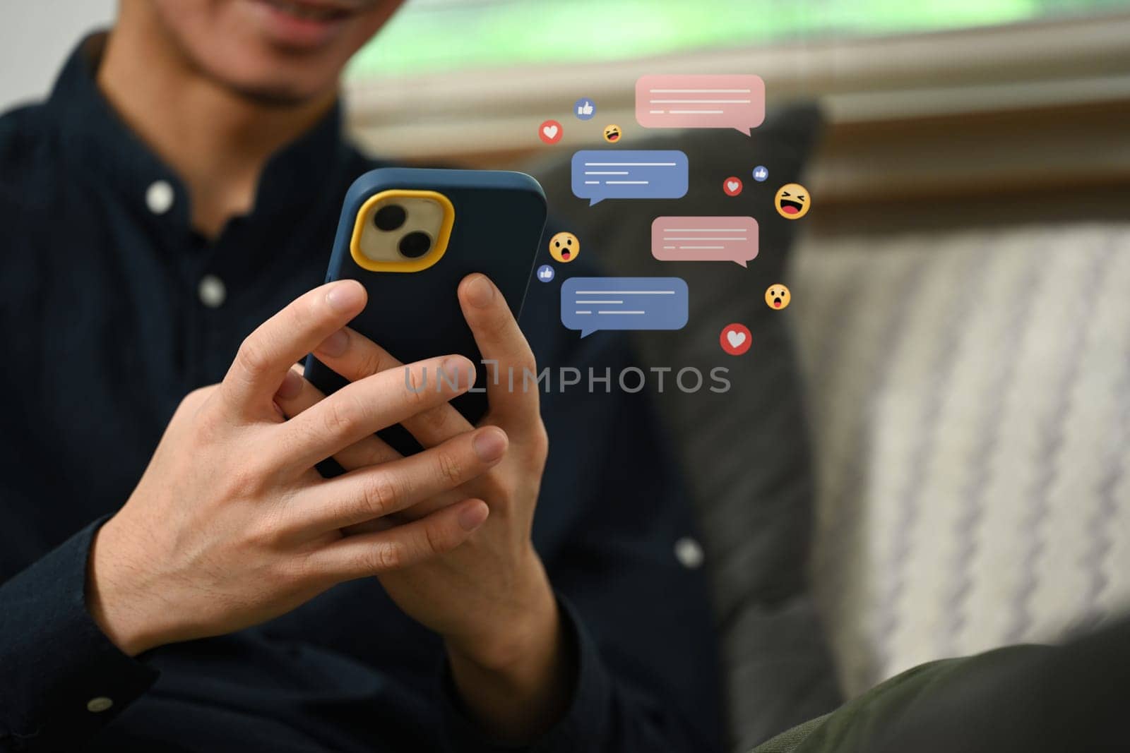 Cropped shot of smiling young man typing text message on smartphone with chatting icons