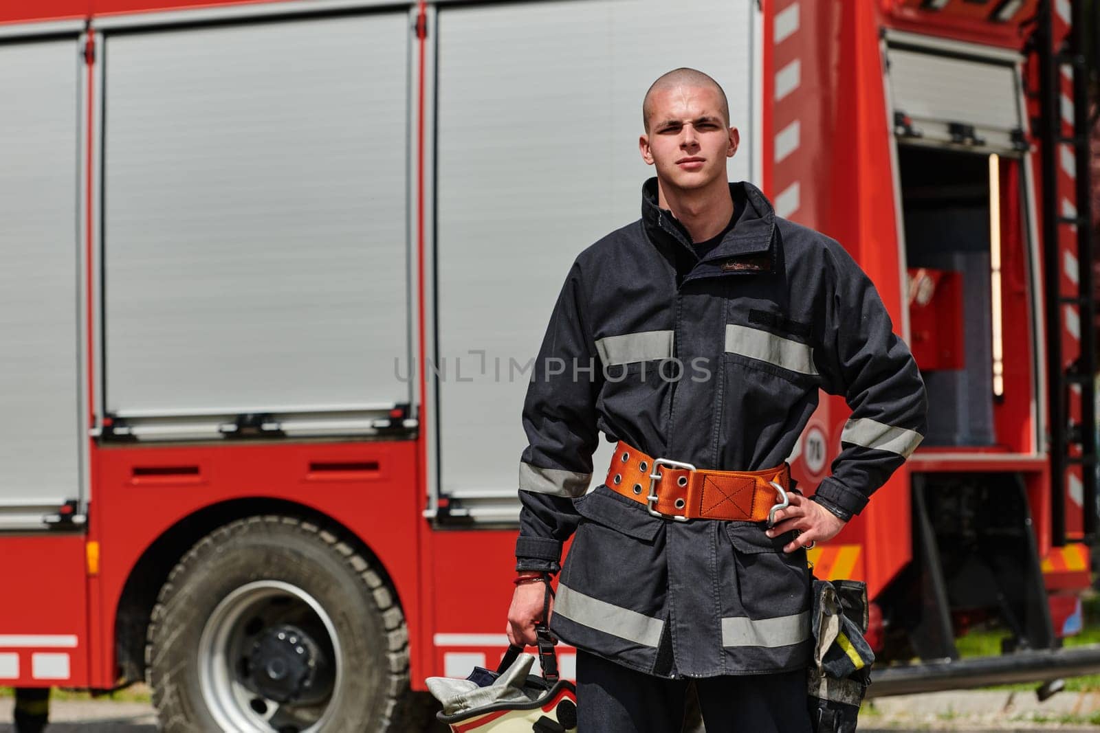 A firefighter, adorned in professional gear, stands confidently beside a fire truck following a grueling firefighting training session