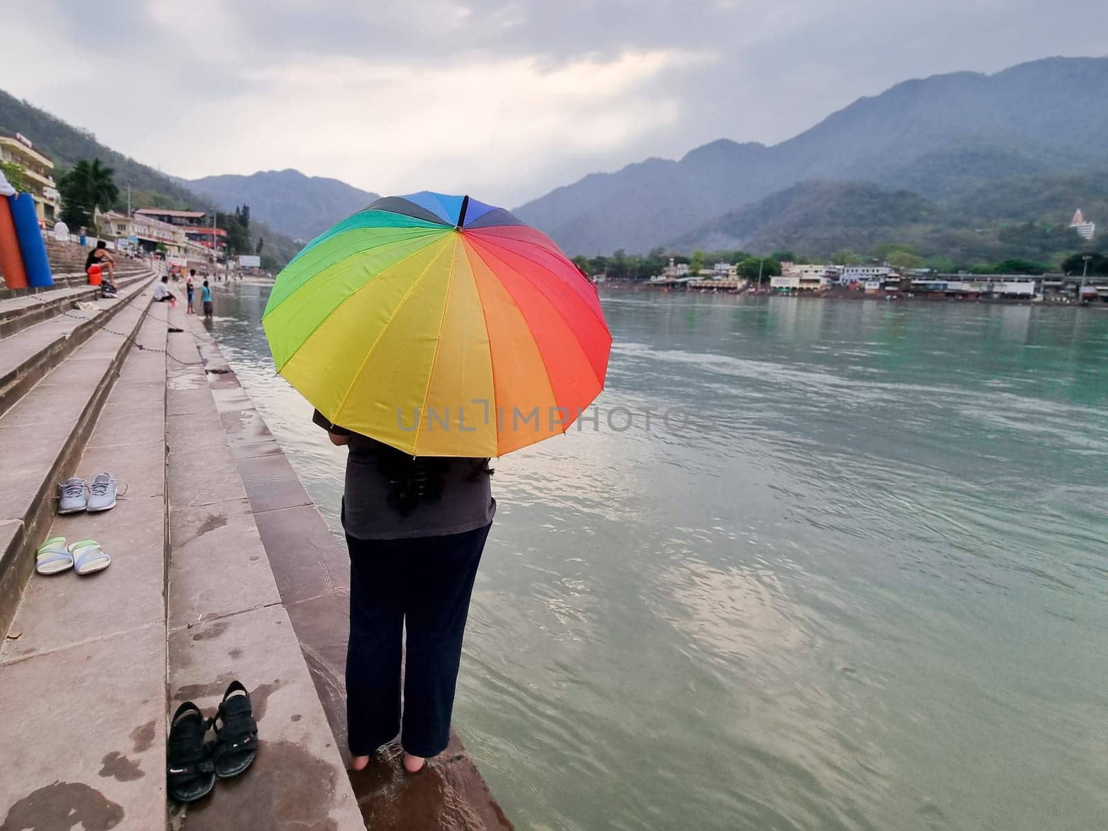 Indian woman standing on the banks of the river ganga on steps with a colorful umbrella and the himalaya mountains in distance in haridwar